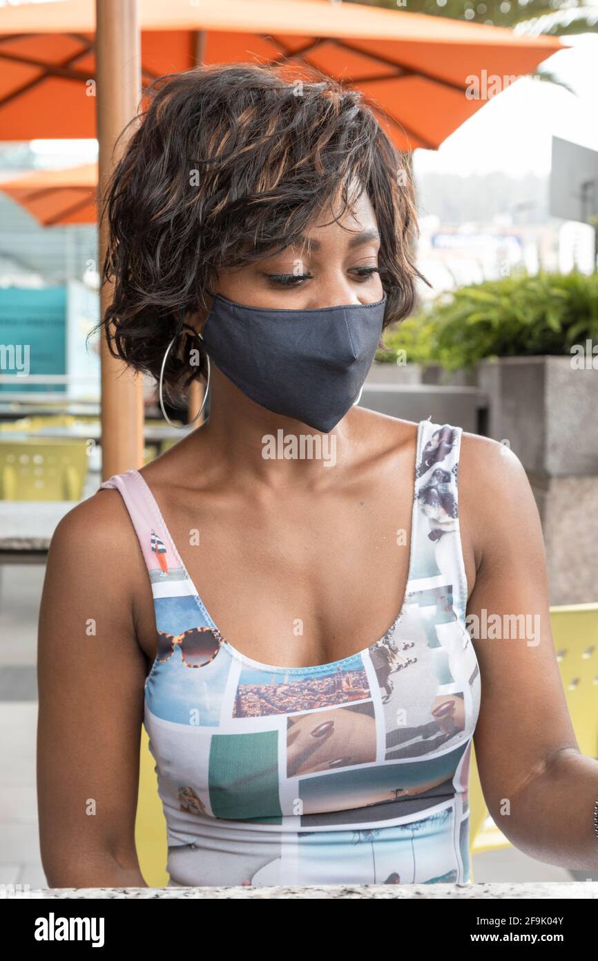 Detail des Gesichts einer afroabhängigen Frau mit kurzen Haaren, im Freien in leichter Kleidung und geschützt mit einer Maske, Schönheit und Modernität Stockfoto