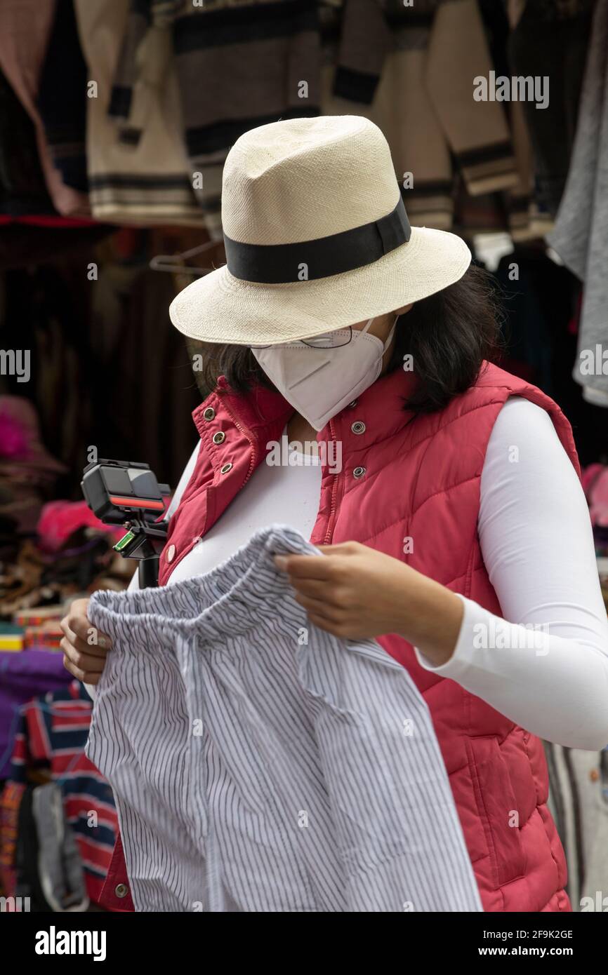 Eine Frau, die in einem Geschäft Kleidung wählt, einen Hut und eine bunte Weste trägt, schaut sich auch eine Hose an und kauft ein Stockfoto
