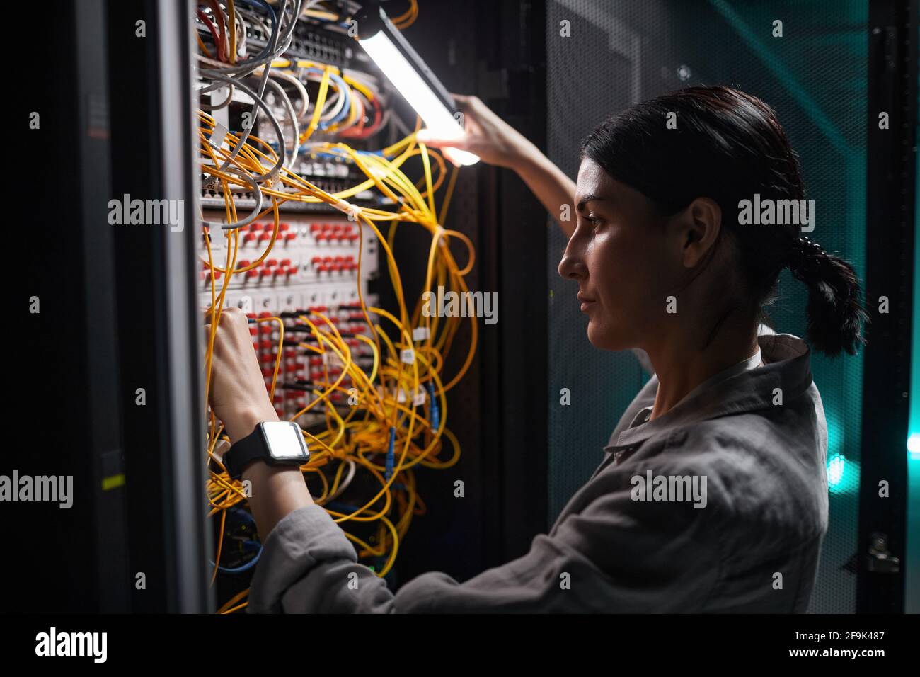 Seitenansicht, Porträt einer weiblichen Netzwerktechnikerin, die Kabel anführt Serverschrank während der Arbeit mit Supercomputer im Rechenzentrum Stockfoto