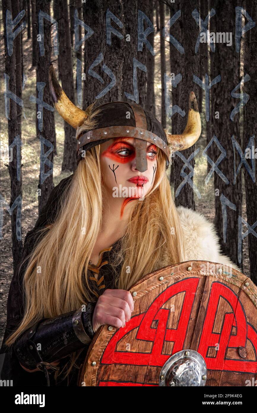 Ein schönes blondes wikingermädchen in einem gehörnten Helm ist Pensiv stehend mit einem Schild auf dem Hintergrund des Gesamtstruktur und Hintergrund des Scans Stockfoto