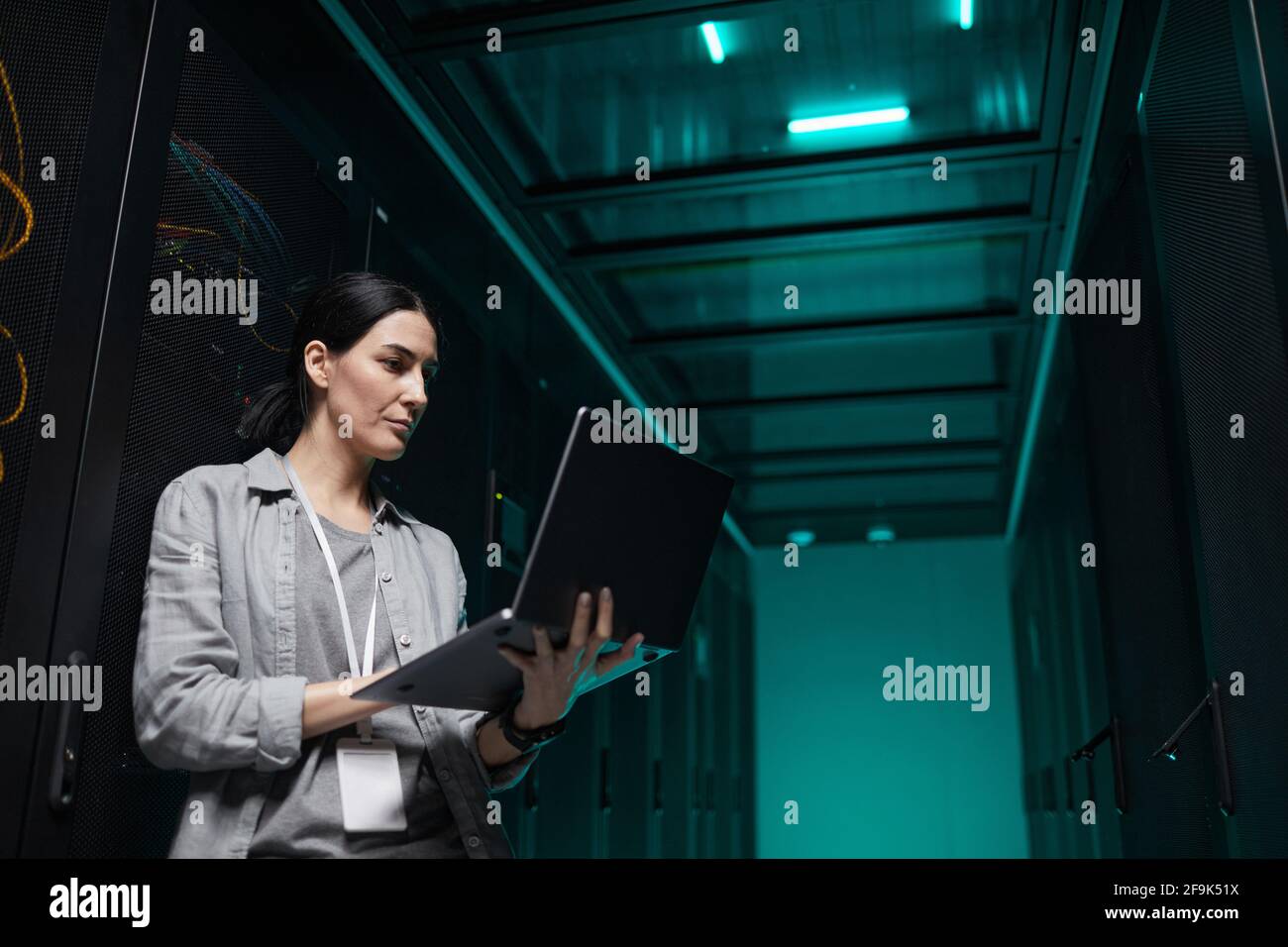 Porträt einer Frau, die einen Laptop in der Hand hält, während sie mit einem Supercomputer im Serverraum arbeitet, und Kopierraum Stockfoto