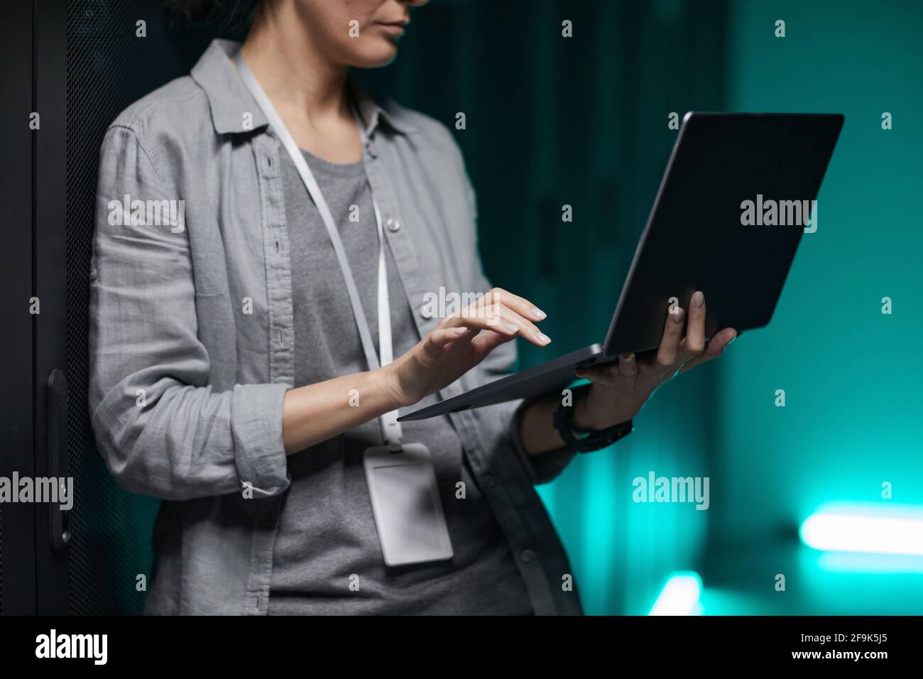 Beschnittenes Porträt einer Frau, die einen Laptop in der Hand hält, während sie mit einem Supercomputer im Serverraum arbeitet, Kopierraum Stockfoto