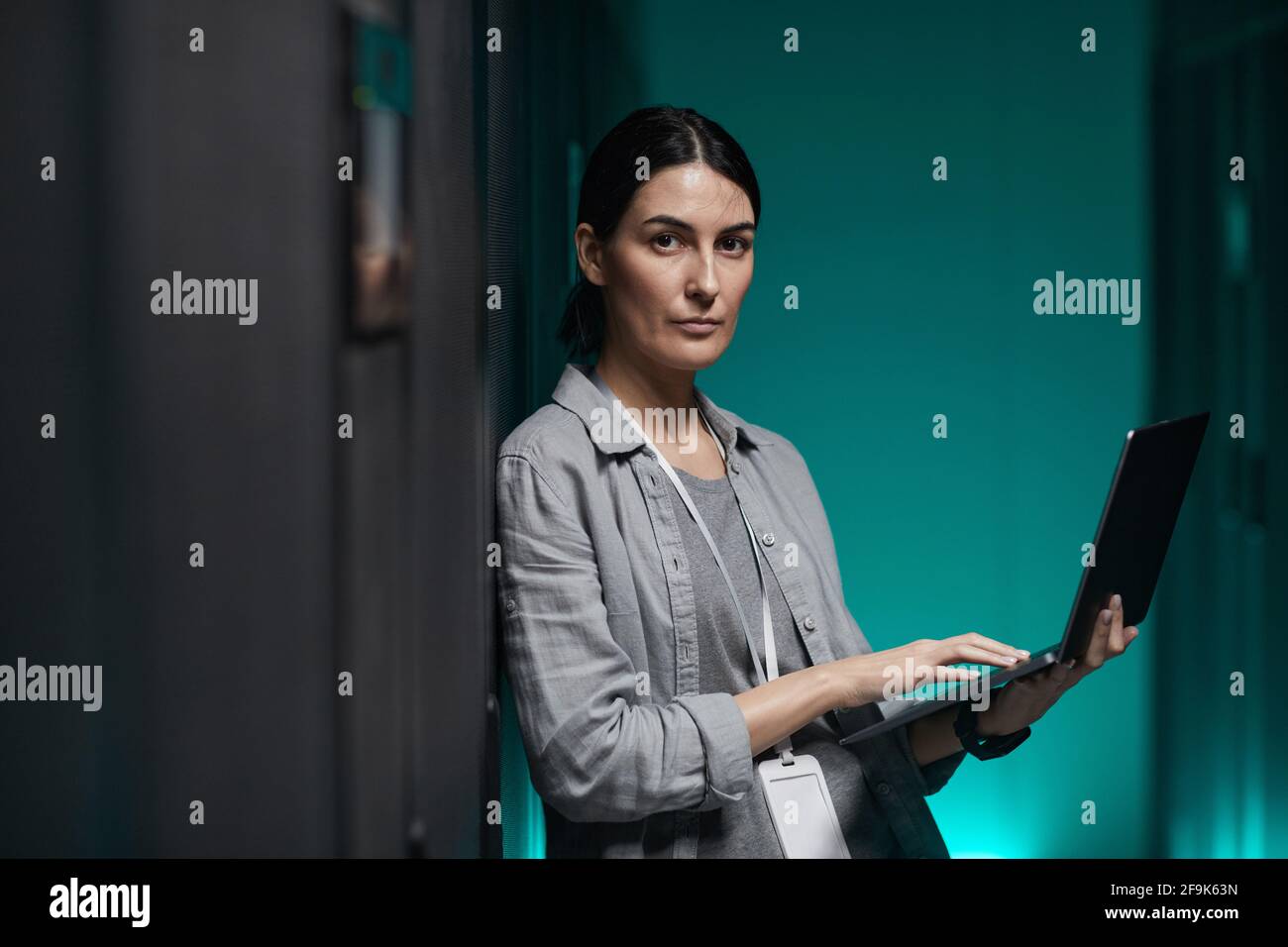 Porträt einer Frau, die einen Laptop in der Hand hält und die Kamera anschaut, während sie mit einem Supercomputer im Serverraum arbeitet und Platz für Kopien hat Stockfoto