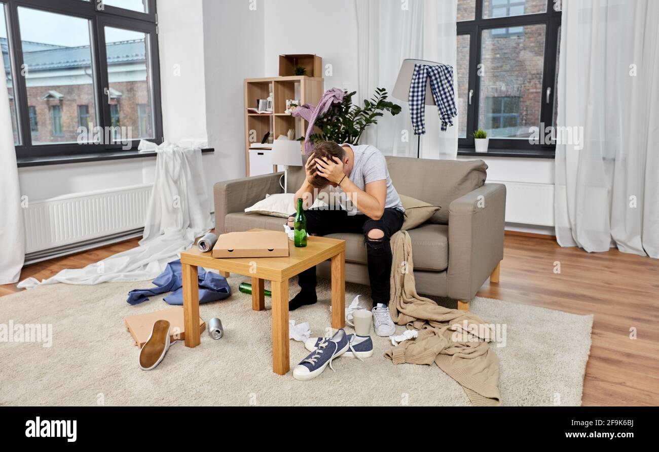 Betrunkener Mann, der zu Hause auf dem Sofa in einem schmutzigen Zimmer sitzt Stockfoto