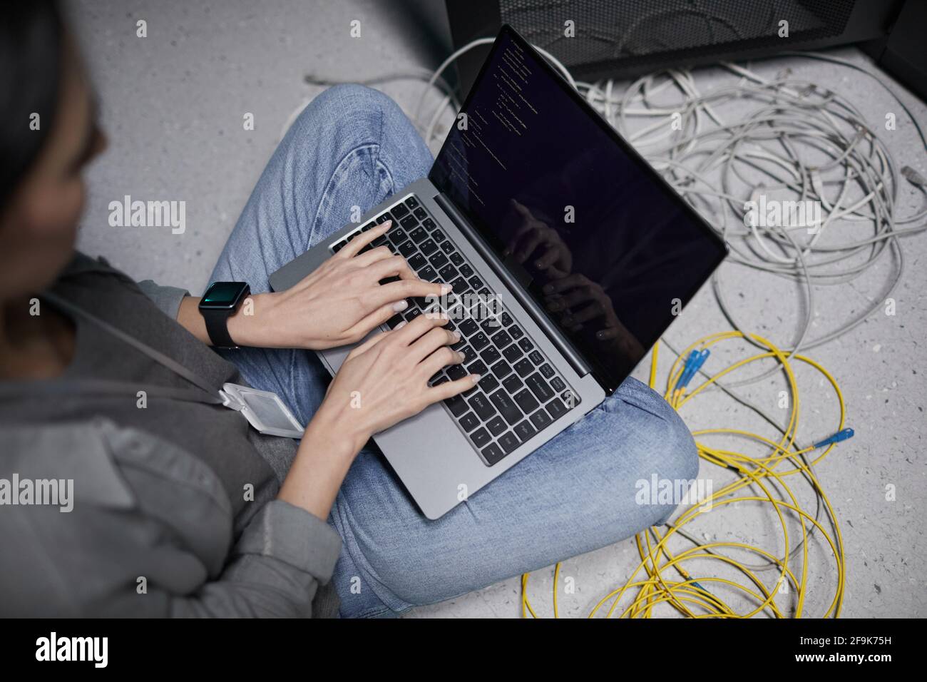 Nahaufnahme einer Frau, die einen Laptop benutzt, während sie im Serverraum auf dem Boden sitzt und ein Supercomputer-Netzwerk aufstellt, und Platz für Kopien Stockfoto