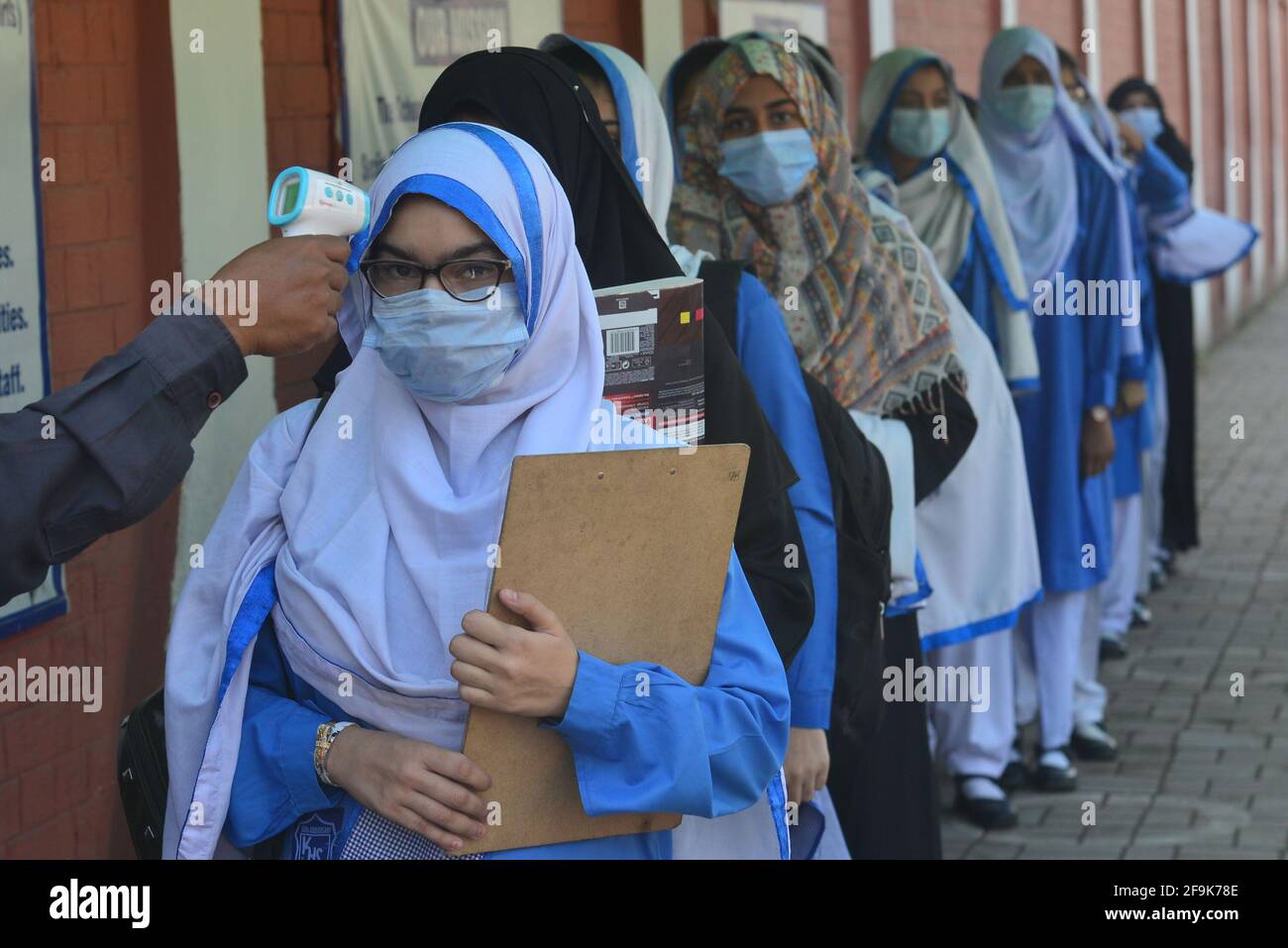 Lahore, Pakistan. April 2021. Ein Sicherheitsbeamter überprüft die Körpertemperatur und desinfiziert die Schuhe von Mädchen, bevor sie in die Bildungseinrichtungen gehen. Die Kinaird-Mädchenschule der Regierung von der 9. Bis 12. Klasse wird nach langen Ferien aufgrund der dritten Phase von Covid-19 in Lahore wieder eröffnet. (Foto von Rana Sajid Hussain/Pacific Press) Quelle: Pacific Press Media Production Corp./Alamy Live News Stockfoto