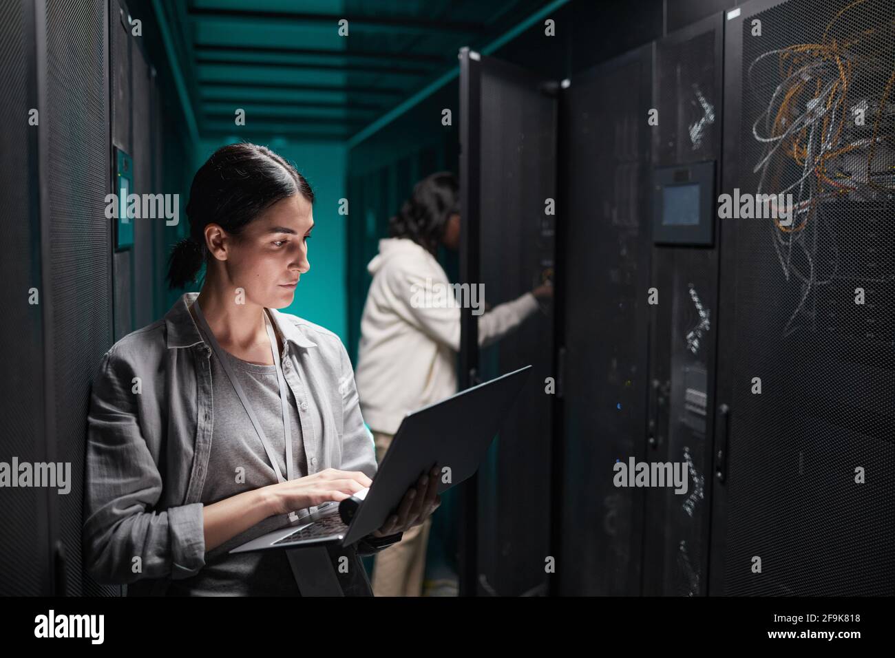 Porträt einer Frau, die einen Laptop im Serverraum benutzt, während sie ein Supercomputer-Netzwerk aufsetzt und Platz kopiert Stockfoto