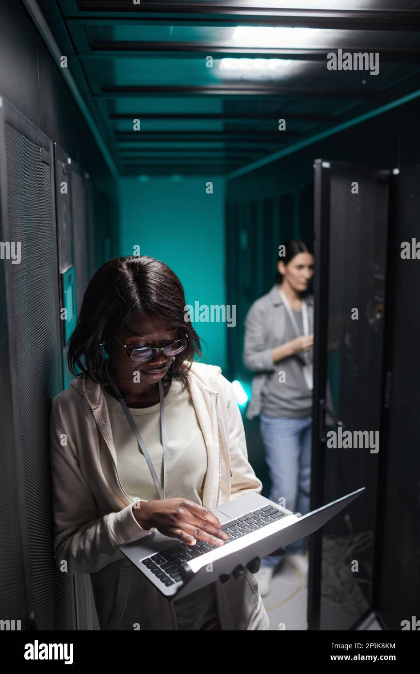 Vertikales Porträt einer Frau, die einen Laptop im Serverraum benutzt, während sie ein Supercomputer-Netzwerk aufstellt, und Platz zum Kopieren Stockfoto