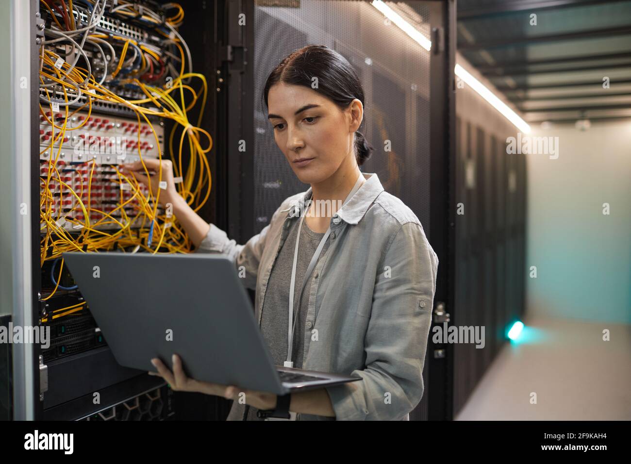Porträt einer weiblichen Netzwerktechnikerin, die Kabel im Serverschrank anschl., während sie im Rechenzentrum mit einem Supercomputer arbeitete, Platz zum Kopieren Stockfoto