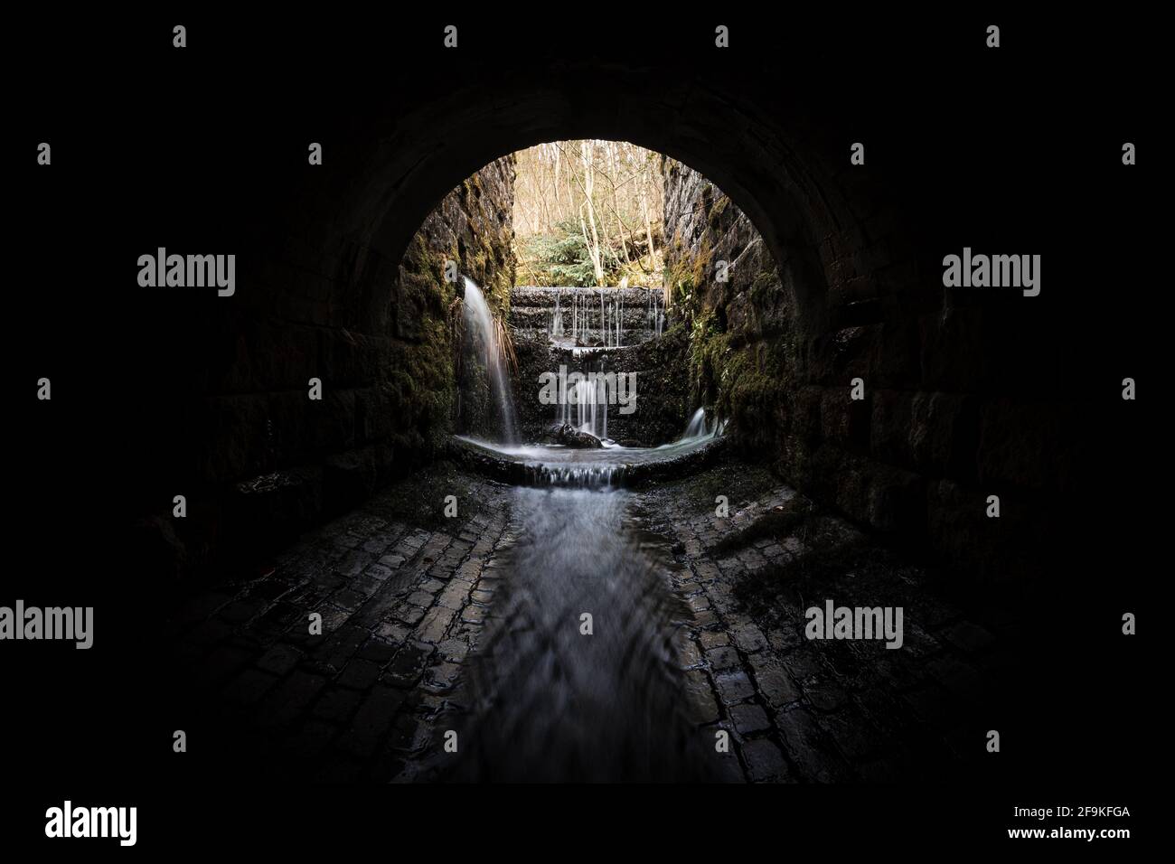 Gruselig dunkel unheimlich alten Kanalisation Backsteintunnel mit gruseligen Schatten Wasser Fluss läuft durch fließendes Licht am Ende. Wasserfälle lange Belichtung verschwommen Stockfoto
