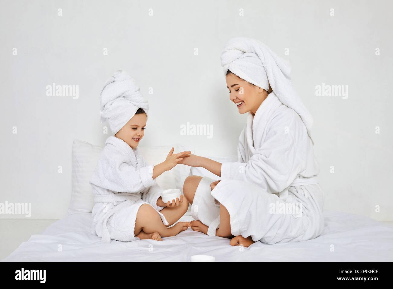 Mutter und Tochter tragen in weißen Bademänteln Creme auf Stockfoto