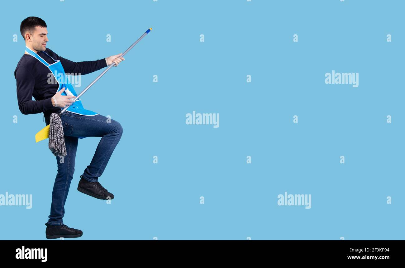 Voller positiver glücklicher Mann, der mit einem Reinigungsmopp auf blauem Hintergrund singt und tanzt, mit viel Platz für Werbung und Textwerbung. Fröhlicher Mann Stockfoto