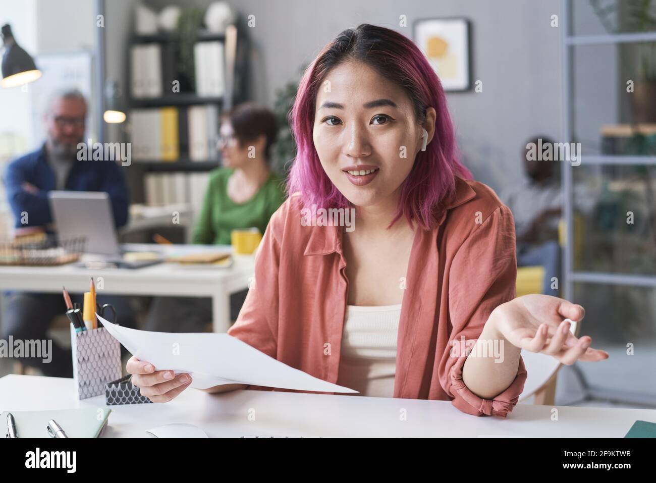 Porträt einer jungen asiatischen Geschäftsfrau, die während der Arbeit die Kamera anschaut Am Tisch mit Dokumenten im Büro Stockfoto