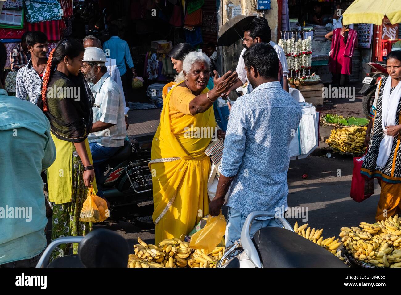 Mysuru, Karnataka, Indien - Januar 2019: Eine indische Straßenverkäuferin mit einem gelben Sari, die auf einem überfüllten Markt in der Stadt mit einem Kunden feilscht Stockfoto