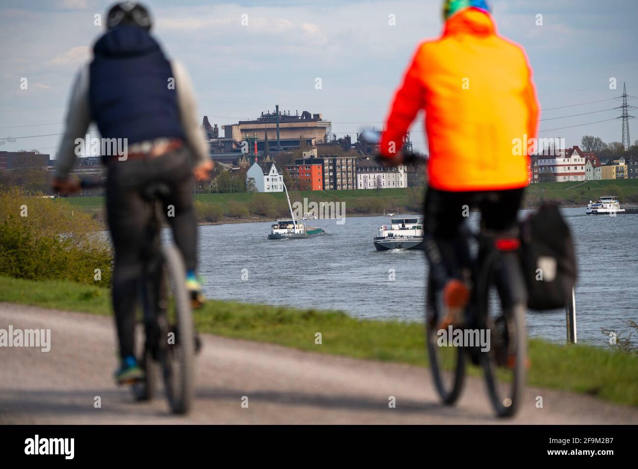 Radfahrer auf dem Rheindeich, Frachtschiffe auf dem Rhein bei Duisburg-Laar, Häuser auf der Deichstraße, industrielle Kulisse des ArcelorMittal Hochfeld GM Stockfoto