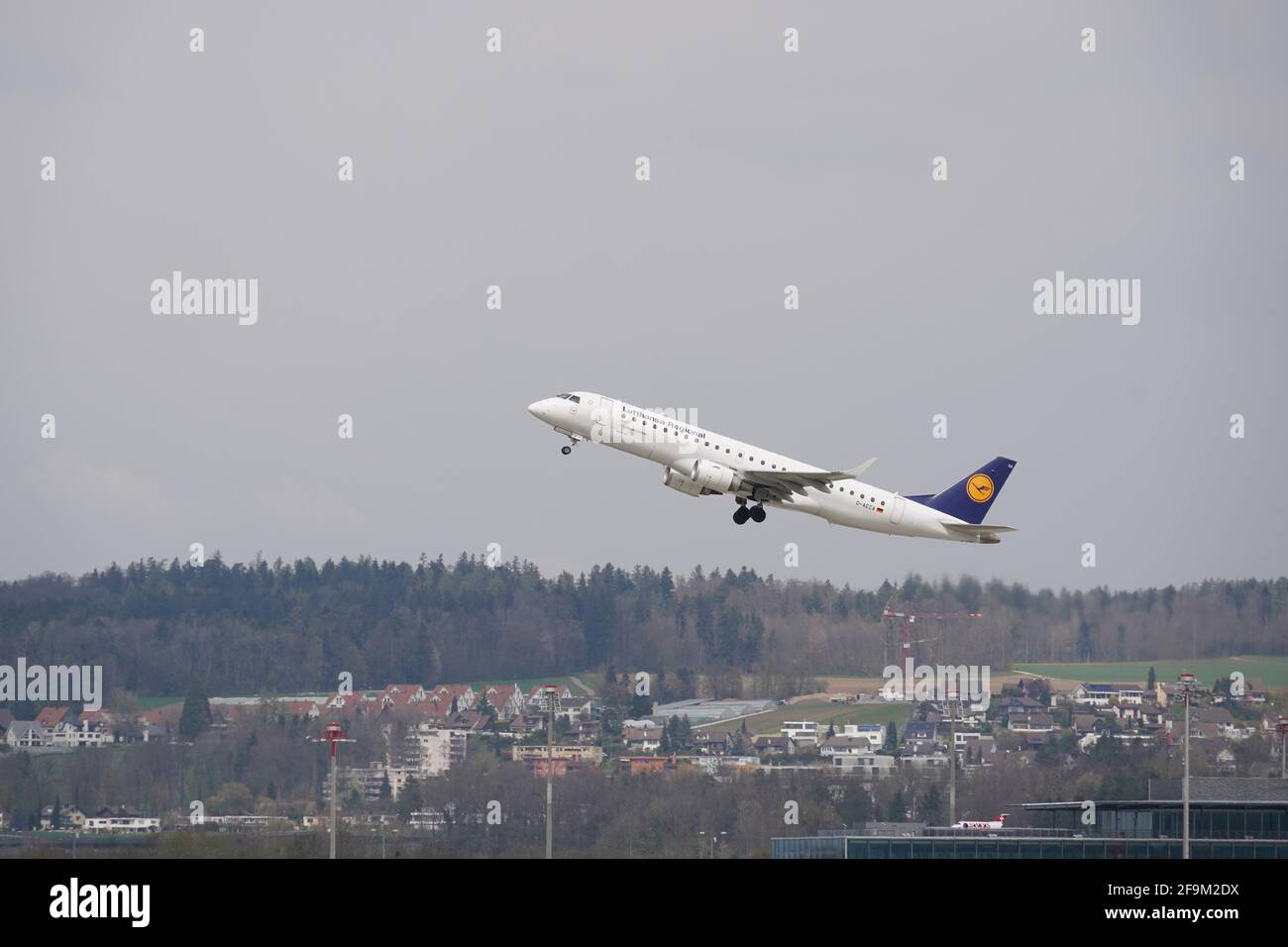Flugzeug der Firma Lufthansa, die vom Flughafen Zürich abfliegt, fliegt über die Gemeinde Kloten nach oben. Auf dem Hintergrund ist der Himmel bedeckt. Stockfoto