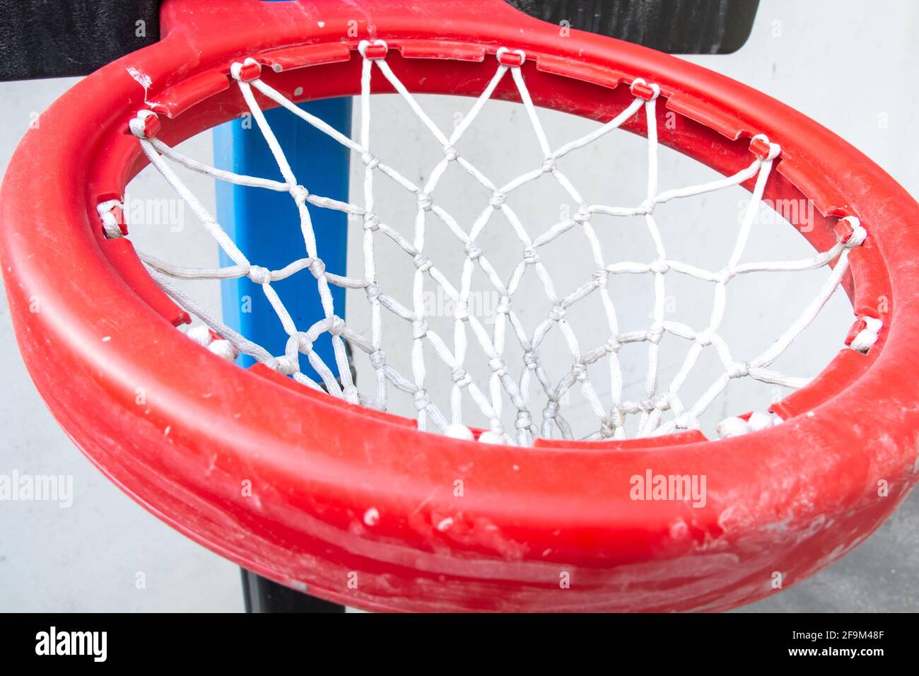 Ein dicker roter Kunststoffring mit weißem Netz, der an einem schwarzen Backboard auf einem Basketballplatz für Kinder befestigt ist. Gedreht in Barbados, Karibik. Stockfoto