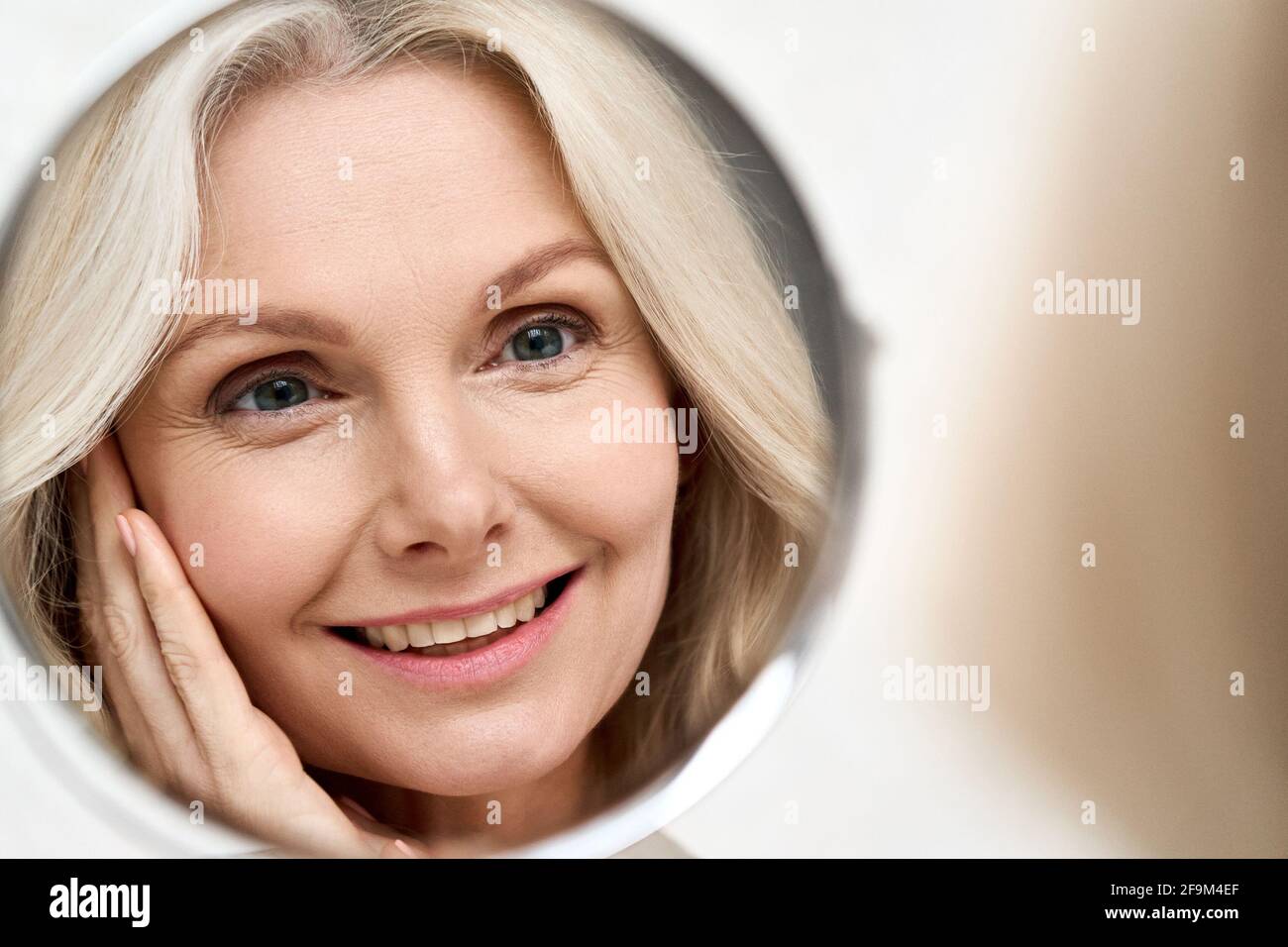 Glückliche Frau mittleren Alters, die den Spiegel ansah. Anti-Aging Beauty Care Konzept. Stockfoto