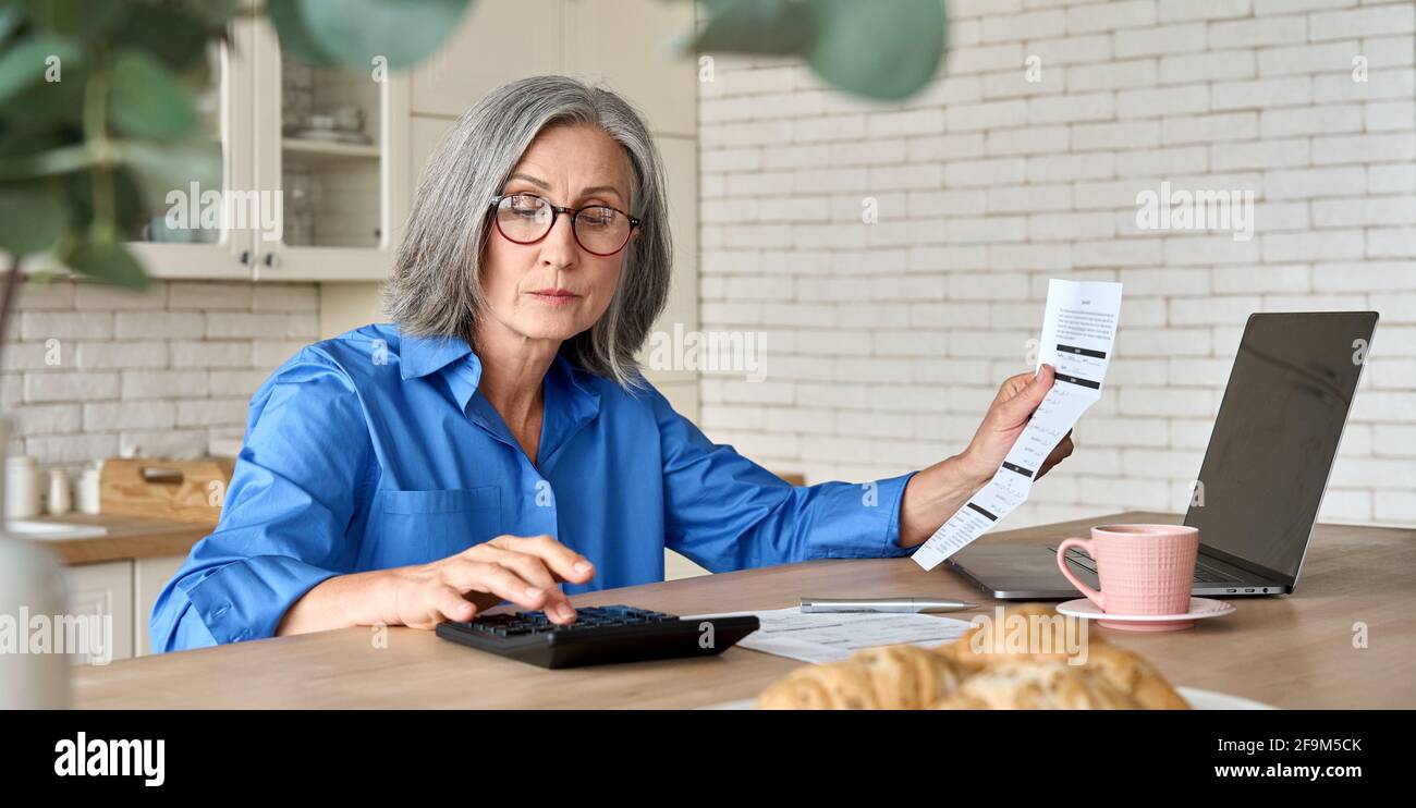 Ältere Frau im Alter von Mitte 60 Jahren, die mit dem Computer Bankgebühren berechnet. Stockfoto