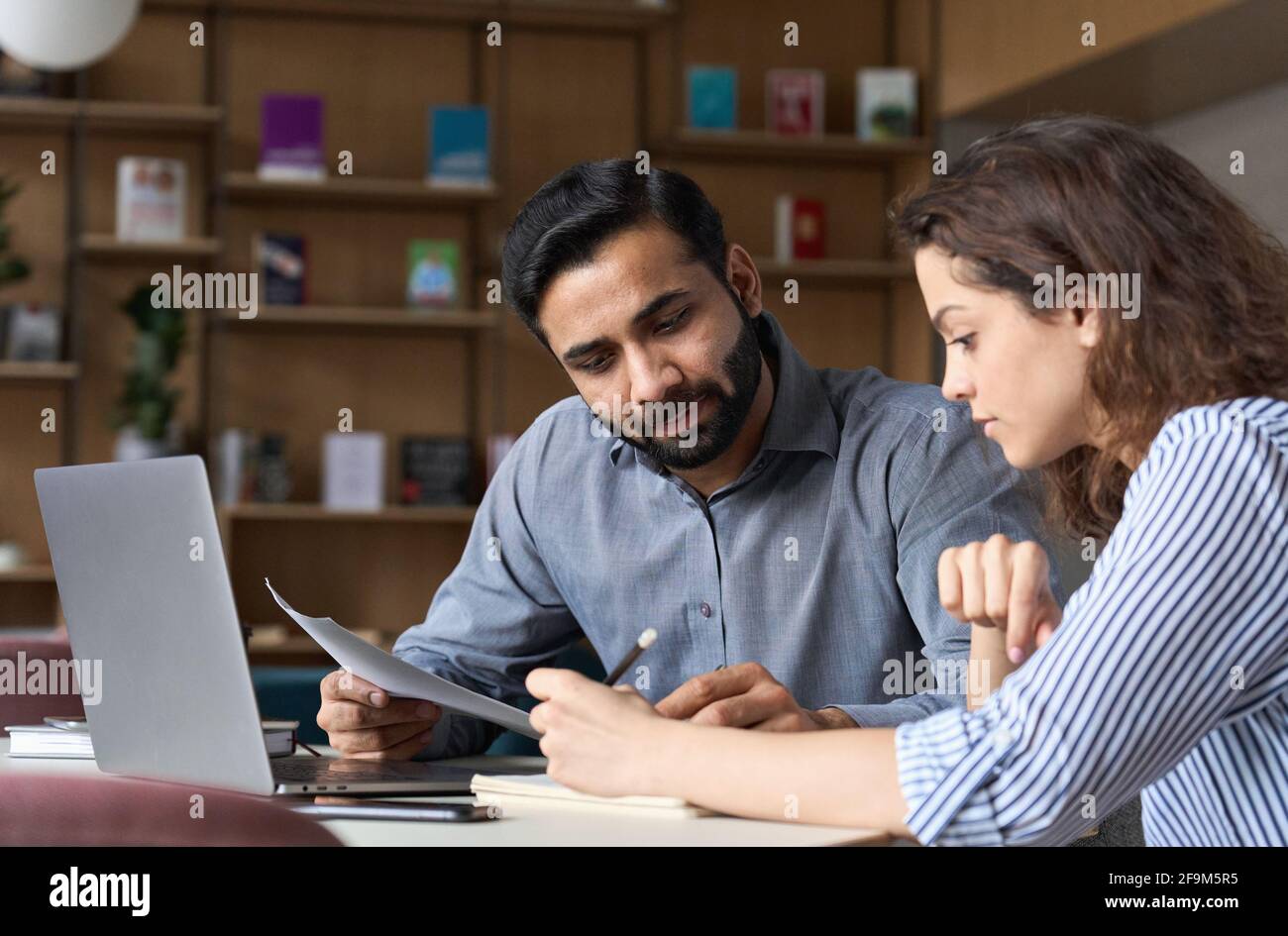 Zwei multiethnische Mitarbeiter arbeiten im Büro mit einem Laptop zusammen. Stockfoto