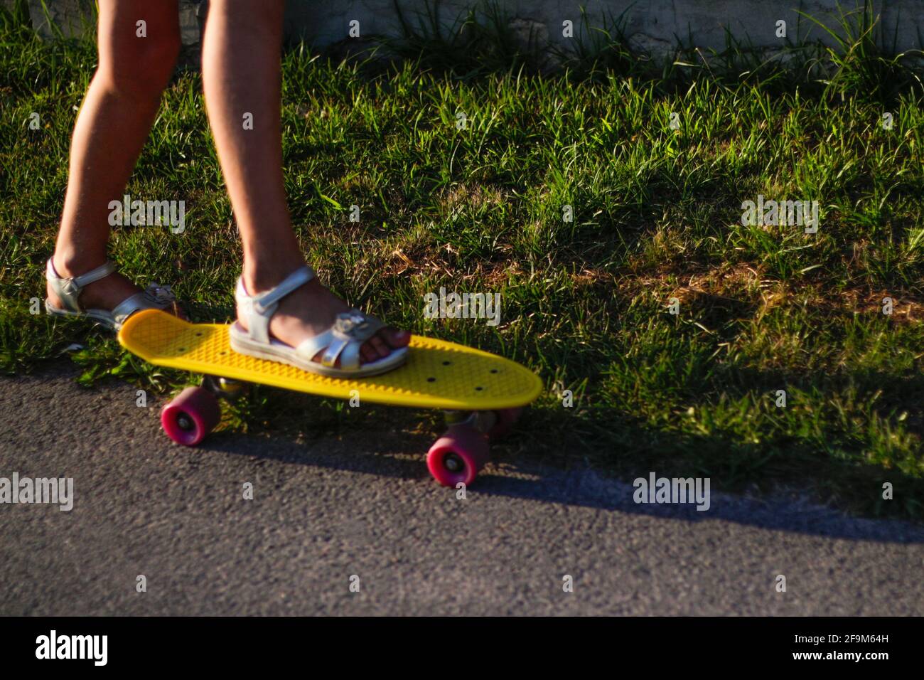 Defocus fit Mädchen in weißen Sandalen bereit, extrem lustig reiten ihr Penny Board Skateboard in Sonnenlicht. Moderne städtische Hipster Mädchen Viel Spaß. Straßenrand und Stockfoto