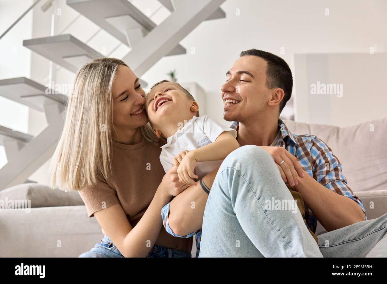 Glückliche junge Erwachsene Eltern mit Kind sitzen auf dem Boden im modernen Wohnzimmer. Stockfoto