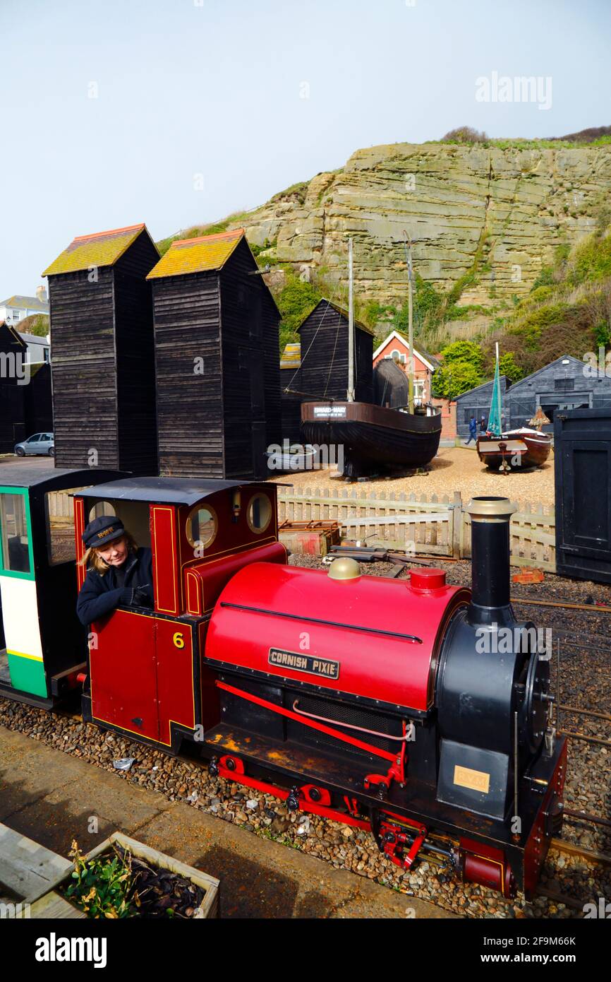 Frau, die mit der Dampflokomotive „Cornish Pixie“ an historischen Holzgeschäften auf der Hastings Miniature Railway, Hastings, East Sussex, England, vorbeifährt Stockfoto