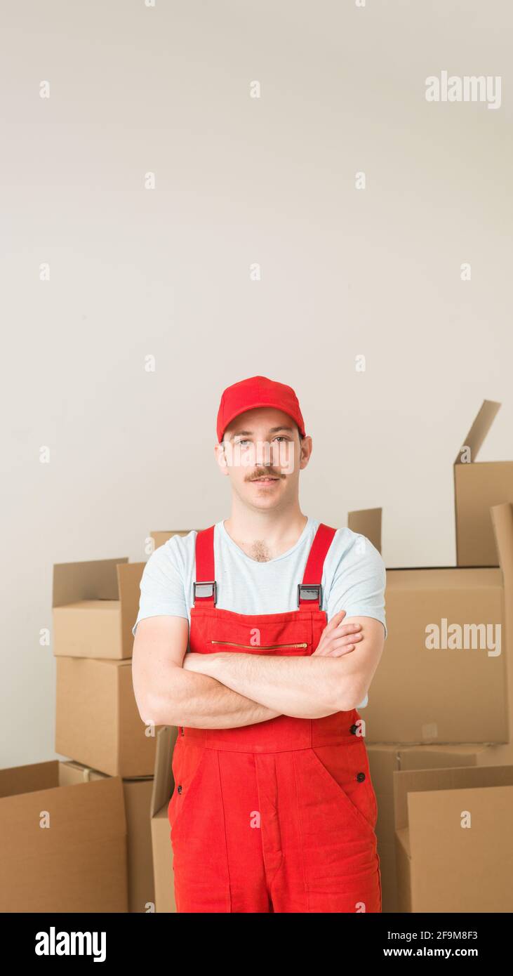 junge zuversichtlich Lieferung Mann stehen, Hand in Hand überquerten gegen seine Brust mit Kartons im Hintergrund Stockfoto