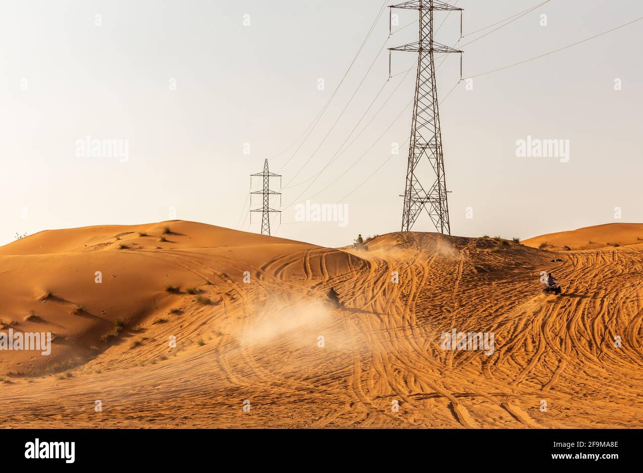 Wenige Dünenbuggys, die die Sanddüne in der Wüste hochfahren, mit elektrischen Türmen im Hintergrund, Sonnenuntergang, Fossil Rock, Sharjah, Vereinigte Arabische Emirate. Stockfoto