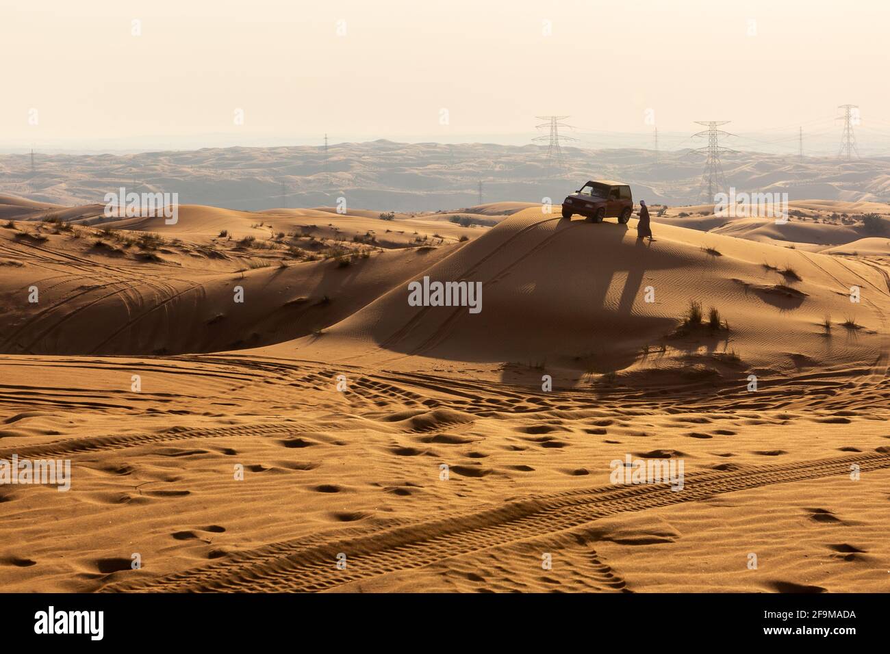 Silhouette eines 4x4-Autos und eines arabischen Mannes in traditioneller Kleidung auf einer Sanddüne bei Sonnenuntergang, Fossil Rock, Sharjah, Vereinigte Arabische Emirate. Stockfoto