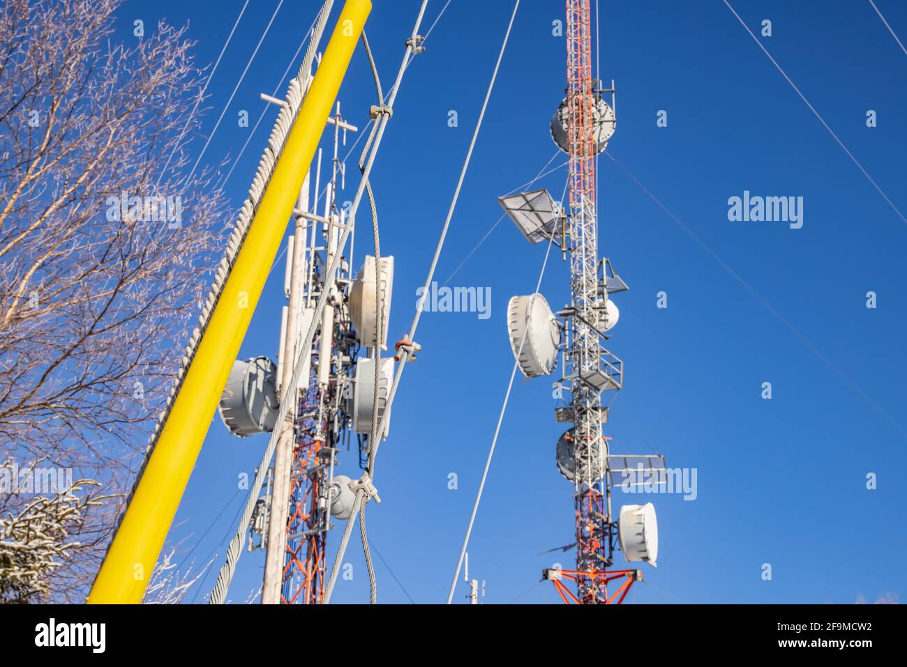 Eine kippbare Aufnahme von zwei Telekommunikationstürmen mit blauem Himmel-Hintergrund, mit denen verschiedene Antennen zur Aufnahme der Funksignale verbunden sind. Stockfoto