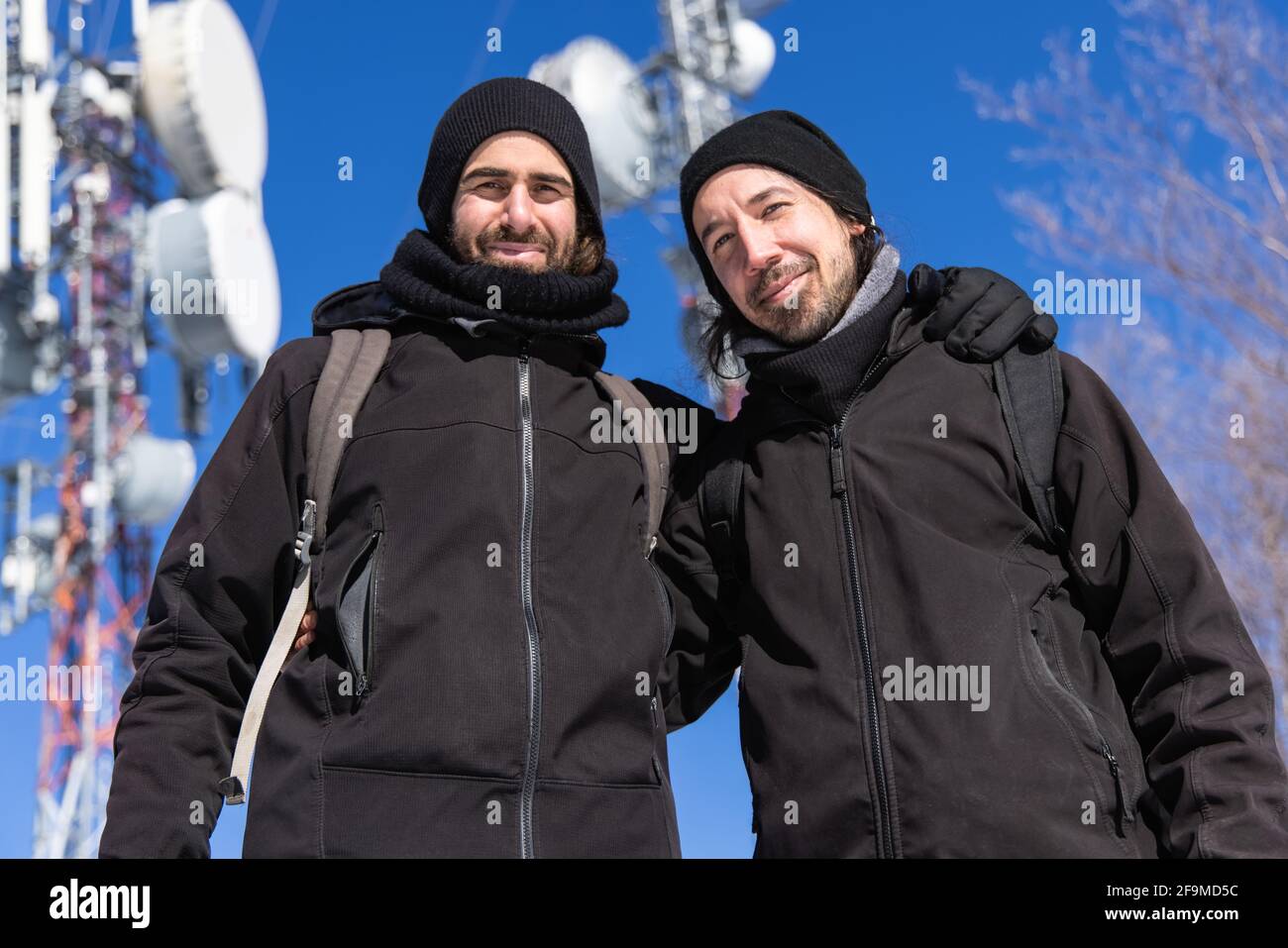 Eine kippbare Aufnahme von zwei Touristen, die in einer verschneiten und kalten Gegend in warmer Kleidung vor den Antennentürmen posieren. Stockfoto