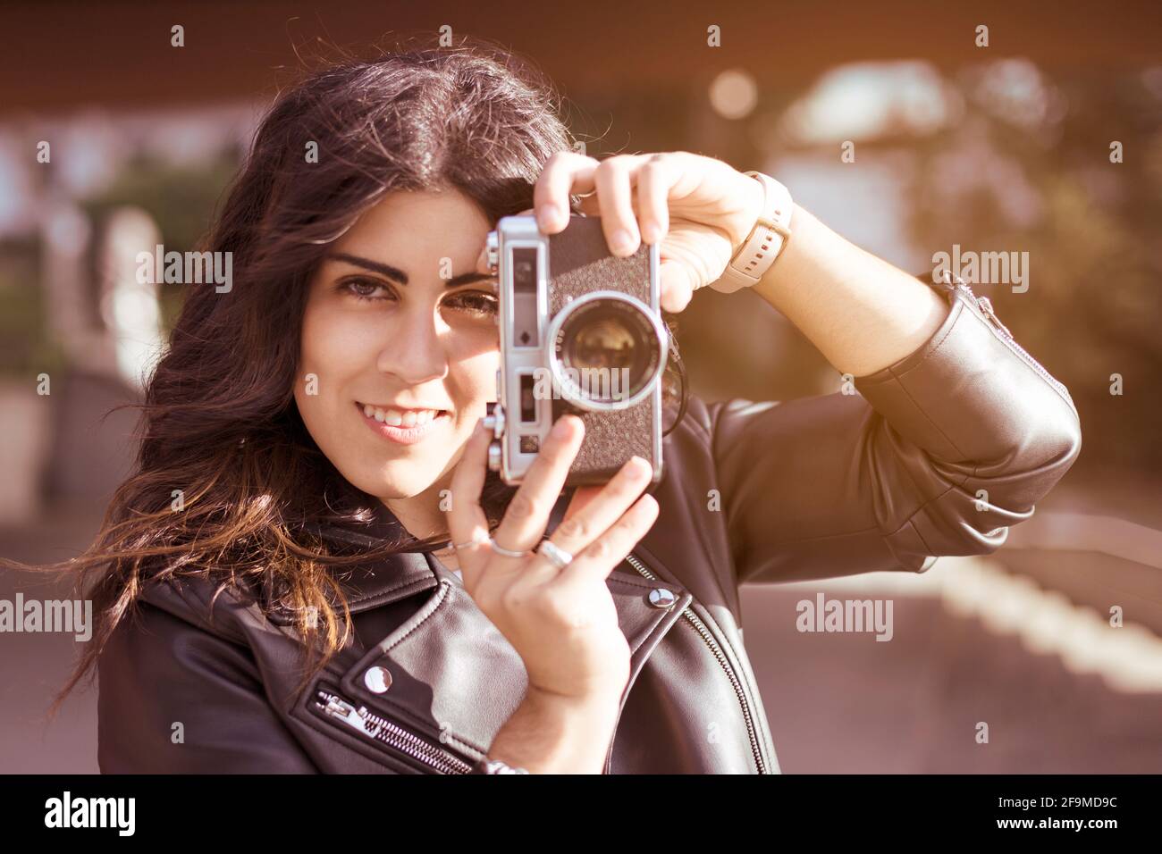 Porträt einer jungen Fotografin, die mit ihrer Analogkamera ein Foto gemacht hat. Sie lächelt in der Stadt und zieht sich lässig an. Platz für Text. Stockfoto