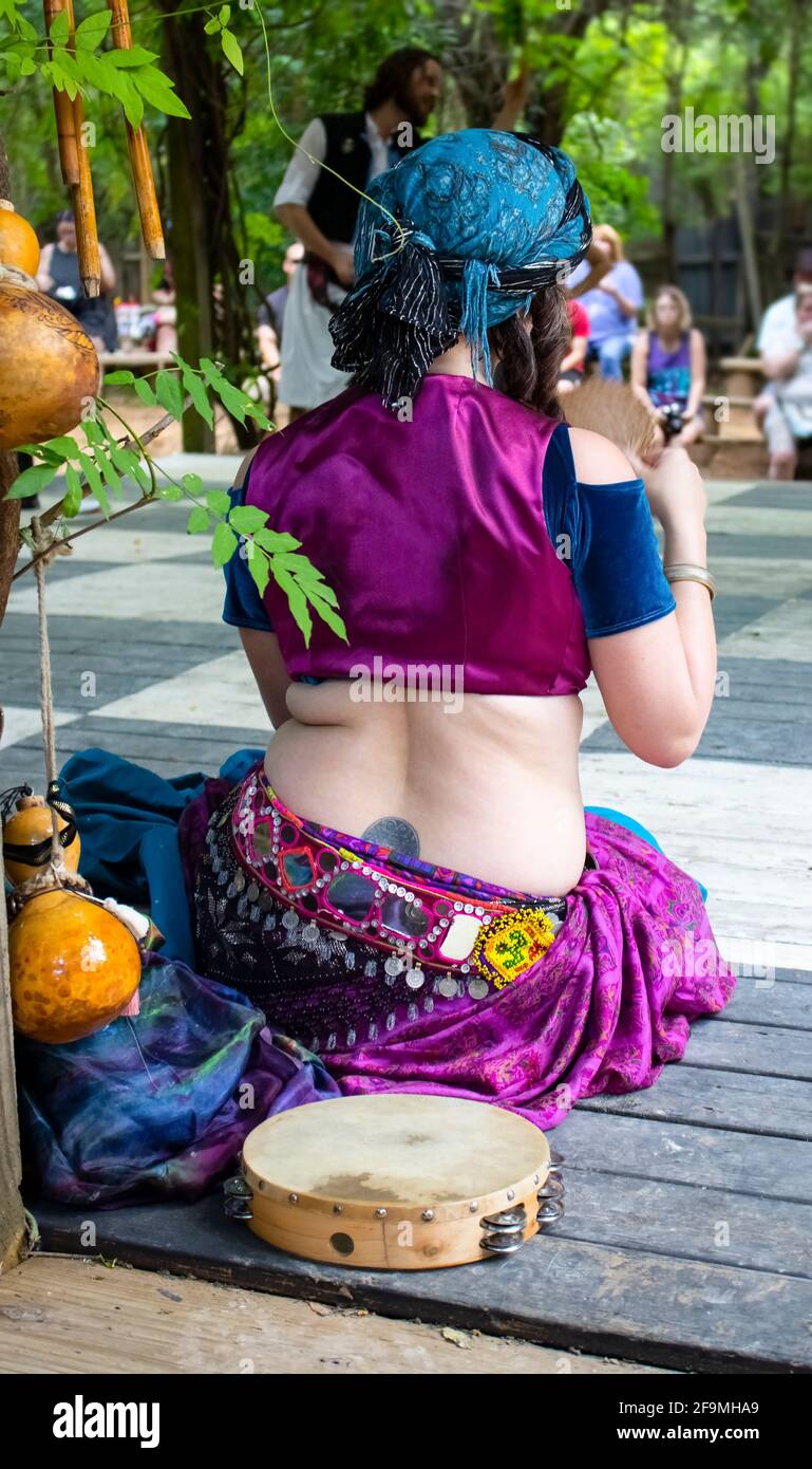 Bauchtänzerin sitzt auf der Seite des hölzernen Outdoor Bühne, nachdem sie mit ihrer tamborine neben ihr tanzte, die sich selbst fächerte Im Renaissance Faire Muskogee Stockfoto