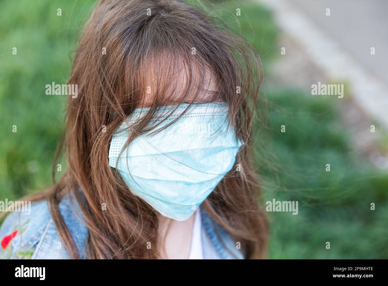 Kleines blondes Mädchen in einer medizinischen Maske und in einer Jeansjacke auf der Straße Stockfoto