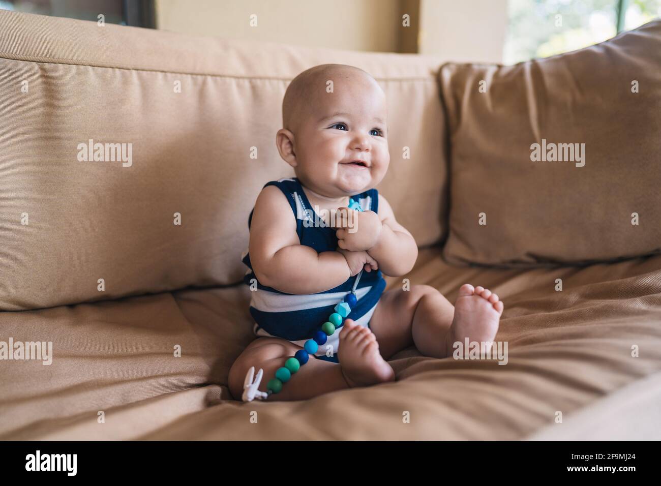 Nettes Baby, das mit einem Spielzeug auf der Couch sitzt Stockfoto