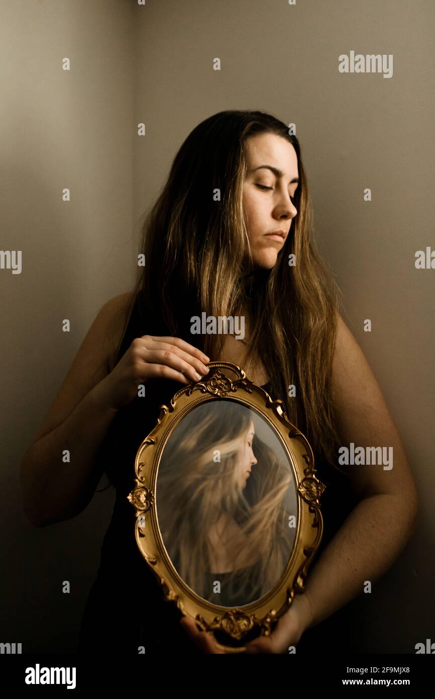 Frau, die einen Vintage-Spiegel in einem Raum mit einem hält Bild von sich selbst. Stockfoto