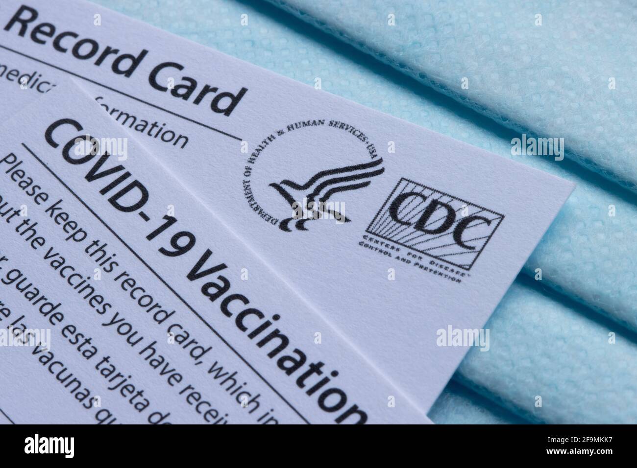 Nahaufnahme der von CDC (United States Centers for Disease Control and Prevention) ausgestellten Covid-19-Impfkarten auf einer blauen Einweg-Gesichtsmaske. Stockfoto