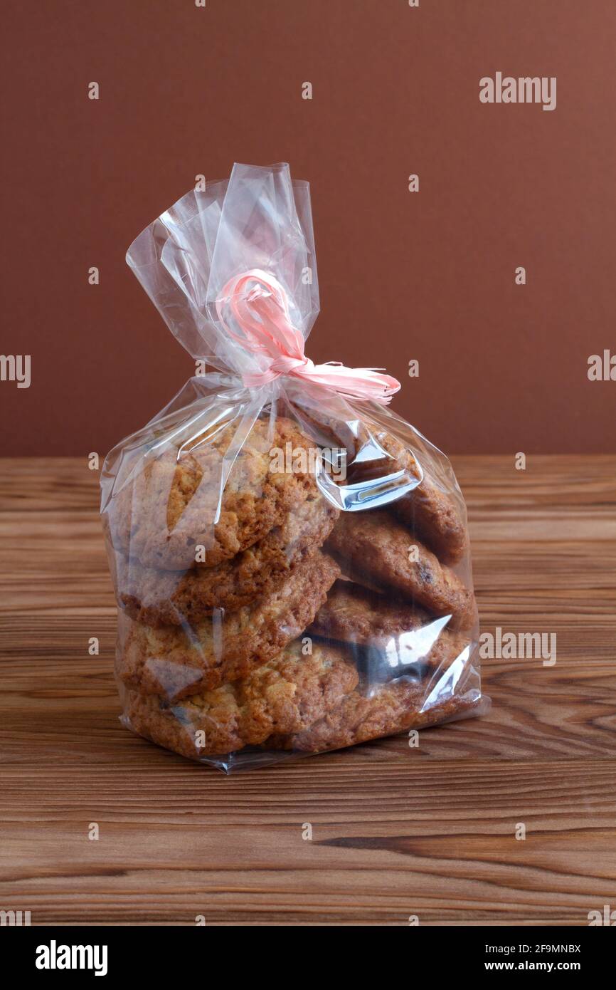 Haferflockenkekse mit getrockneten Preiselbeeren in durchsichtigem Beutel auf einem Holztisch an einer braunen Wand. Nahaufnahme. Makro Stockfoto