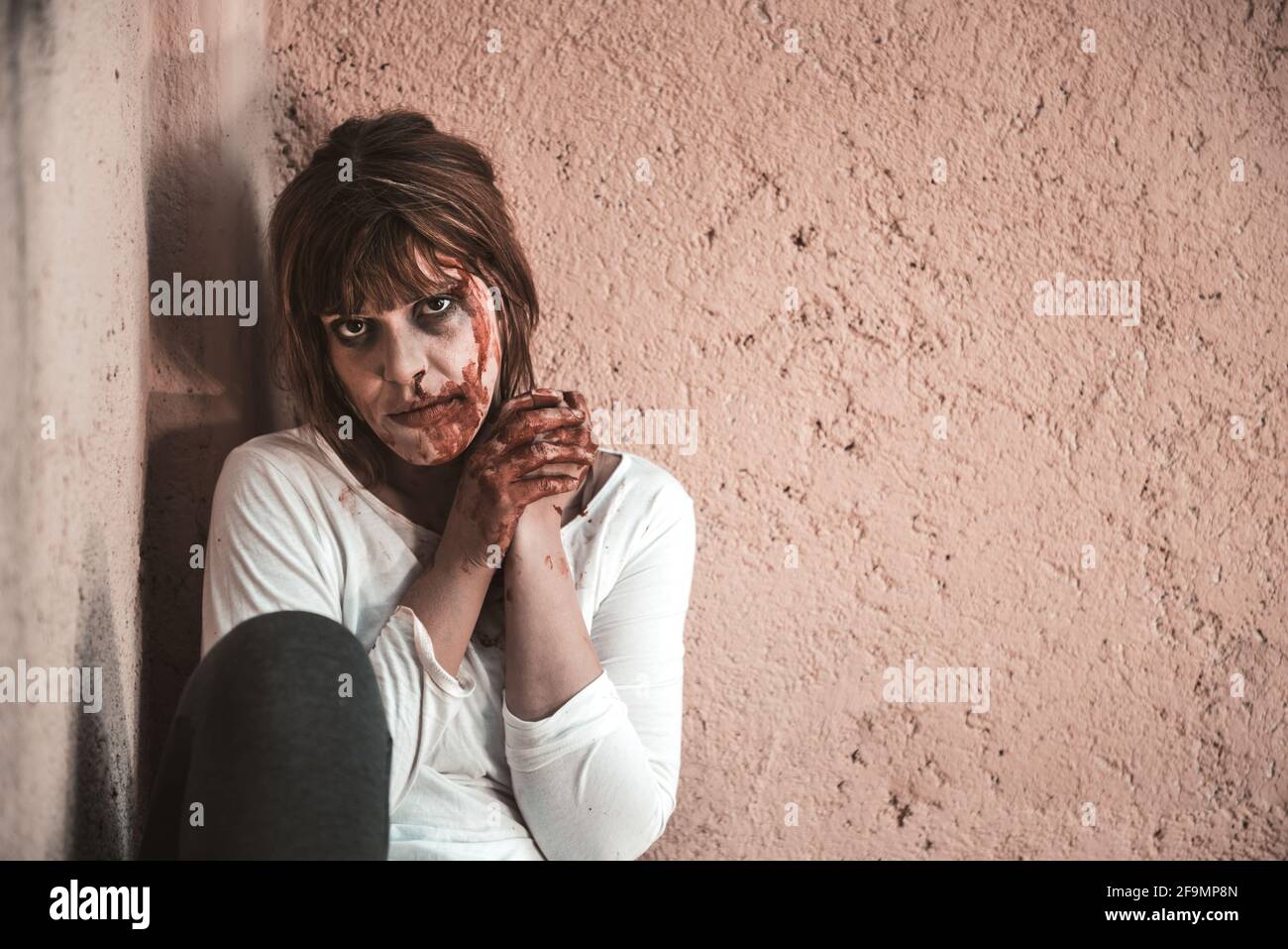Ein hockendes Mädchen vor einer schmutzigen Wand, verzweifelt, weinend und verwundet Mädchen, das sie mit einem traurigen Blick sieht, sie ist auf dem Boden auf einem Bürgersteig. Stockfoto