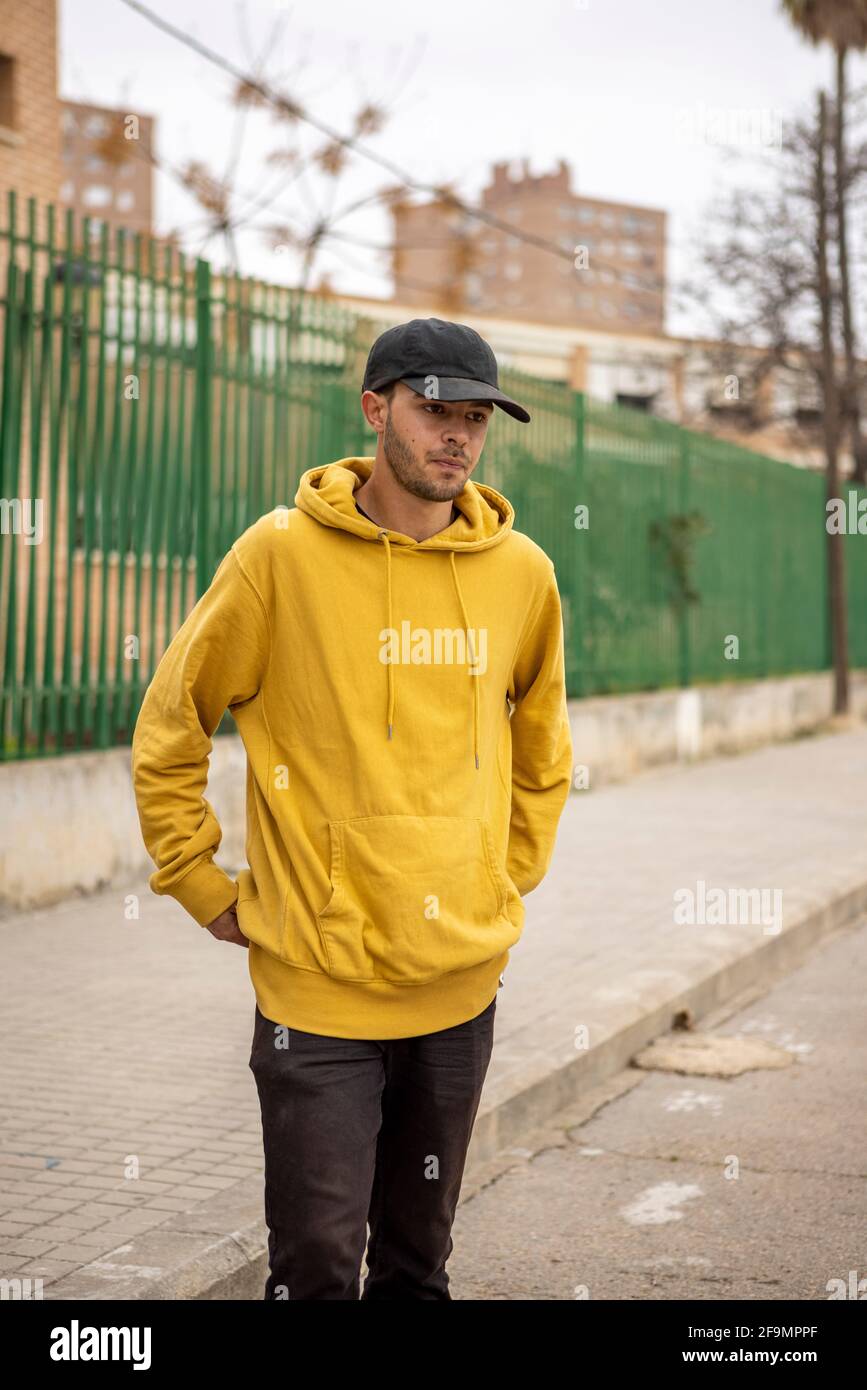 Junger kaukasischer Rüde mit gelbem Hoodie und schwarzer Mütze Auf der Straße stehen Stockfoto