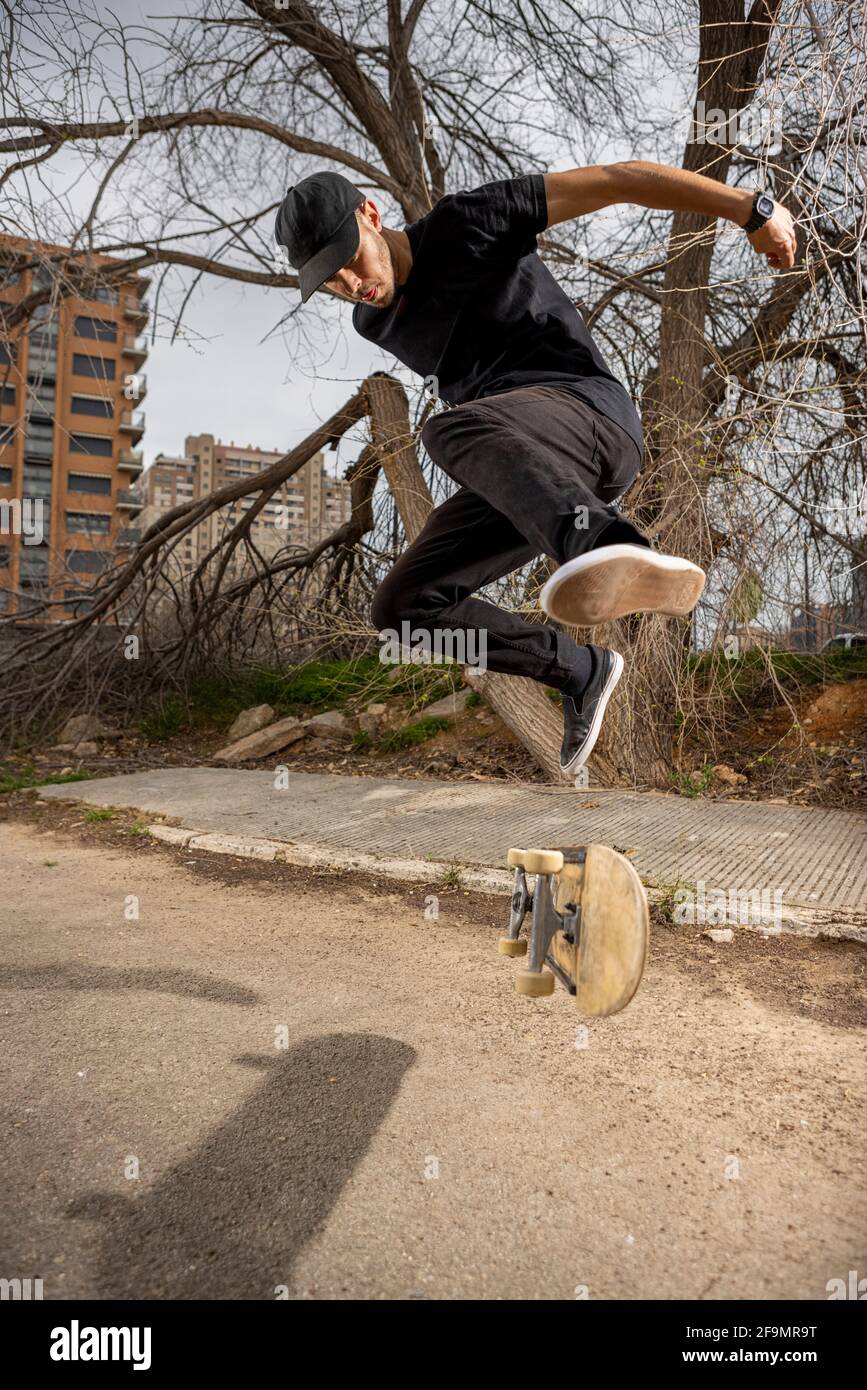 Junger kaukasischer Rüde in einem schwarzen Hemd und einer Mütze, die springt Mit seinem Skateboard Stockfoto