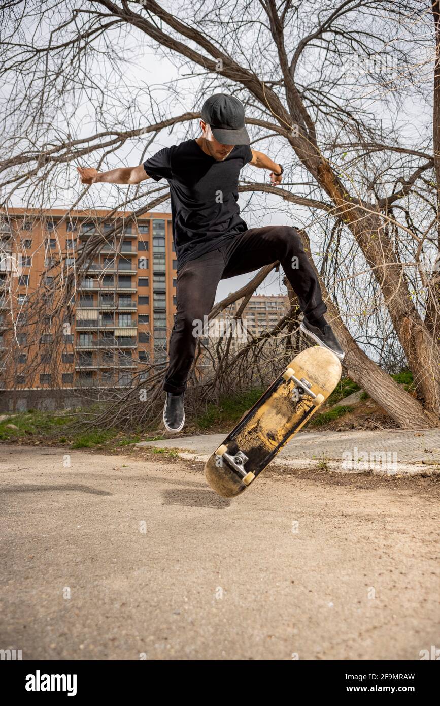 Junger kaukasischer Rüde in einem schwarzen Hemd und einer Mütze, die springt Mit seinem Skateboard Stockfoto