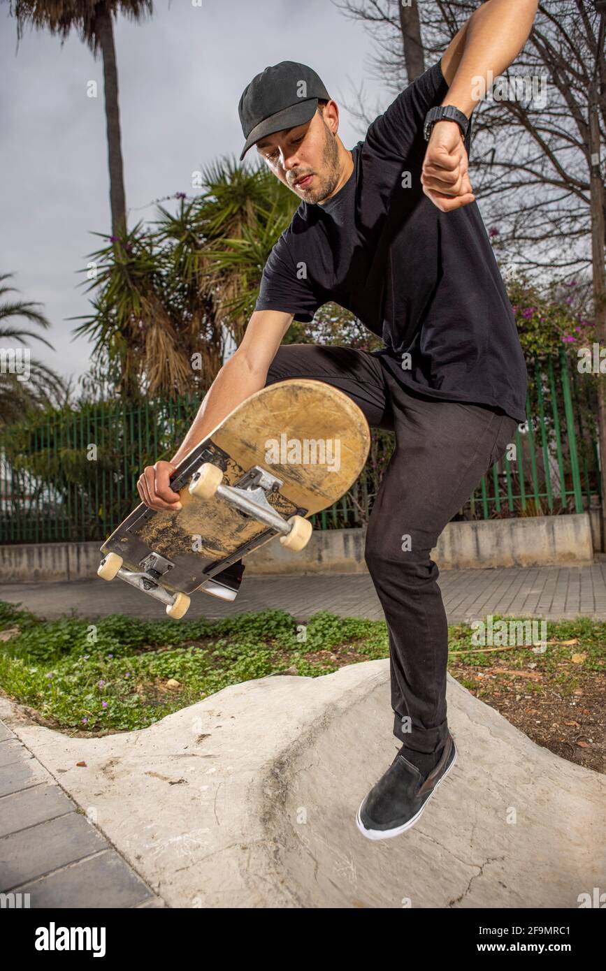 Junger kaukasischer Rüde in einem schwarzen Hemd und Mütze Springen mit seinem Skateboard Stockfoto