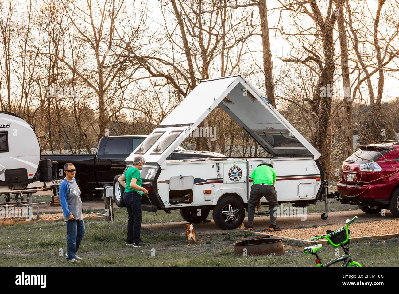 LIMESTONE, TN, USA--8 APRIL 2021: Ein Wohnmobil-Campingplatz, auf dem ein Mann einen A-Rahmen-Campinganhänger aufmacht, auf dem zwei Frauen zuschauen. Frühmorgens. Stockfoto
