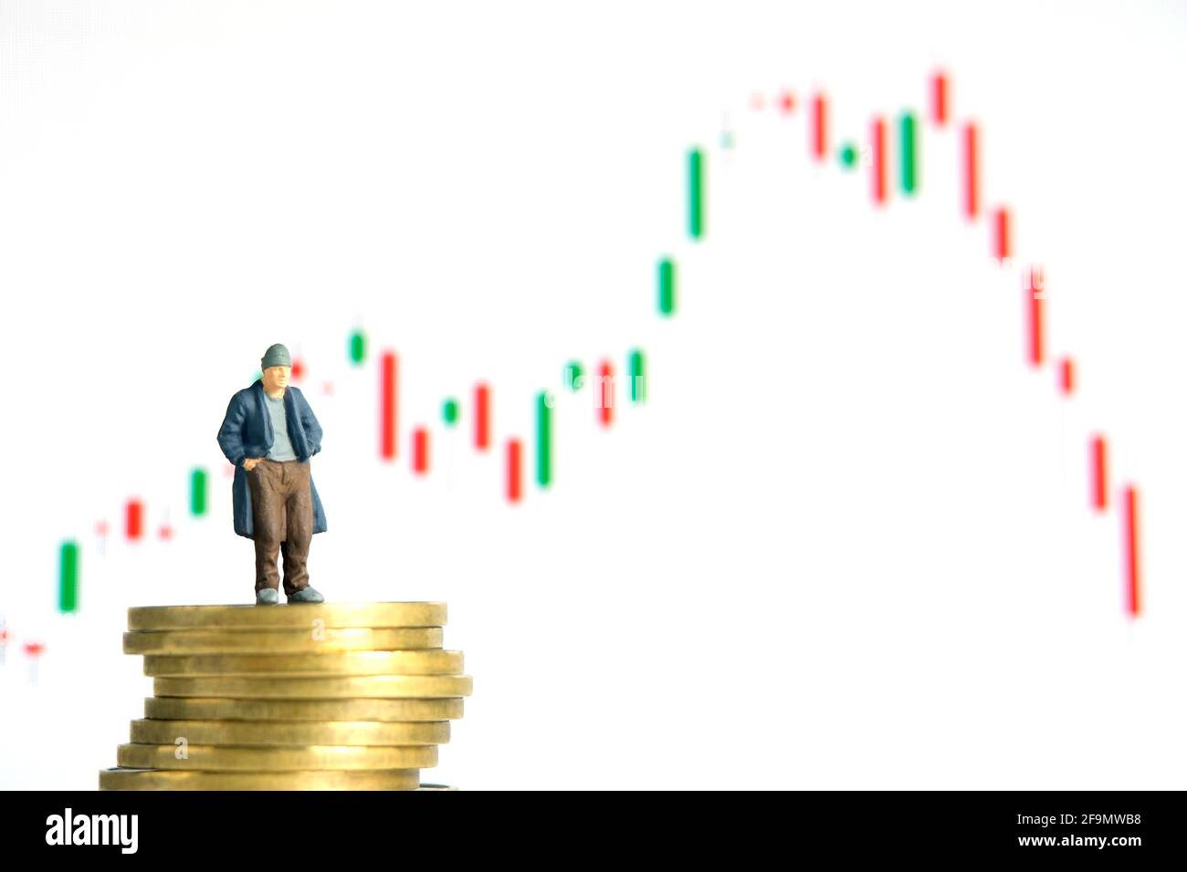 Miniatur kleine Menschen Spielzeug Fotografie. Die Menschen, die über dem Münzstapel stehen, haben kein Geld oder sind bankrott, die Aktienmarkt-Candle-Chart fiel herunter, isolieren Stockfoto