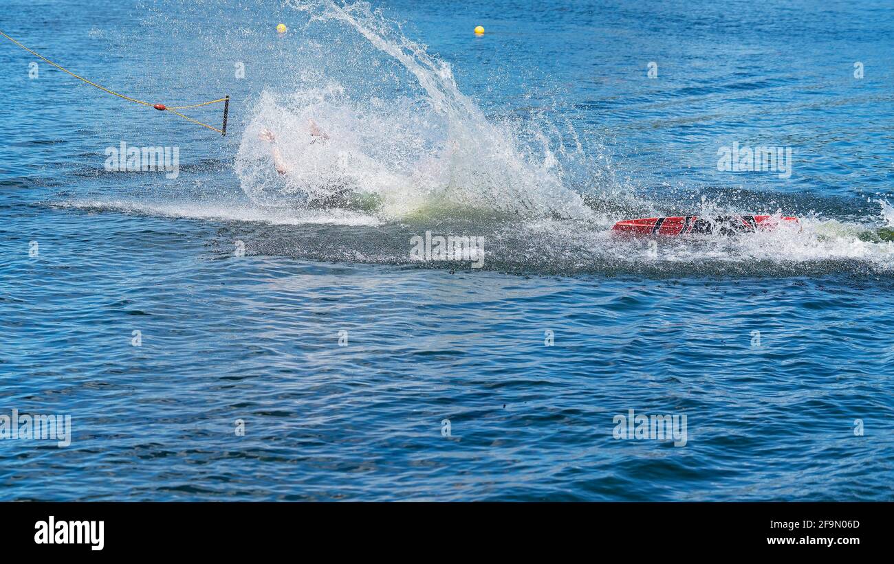 Mann, der in einem Seilschipark Wakeboard lernt und Es gelingt ihm nicht, als er mit einem Spritzer abfällt Stockfoto