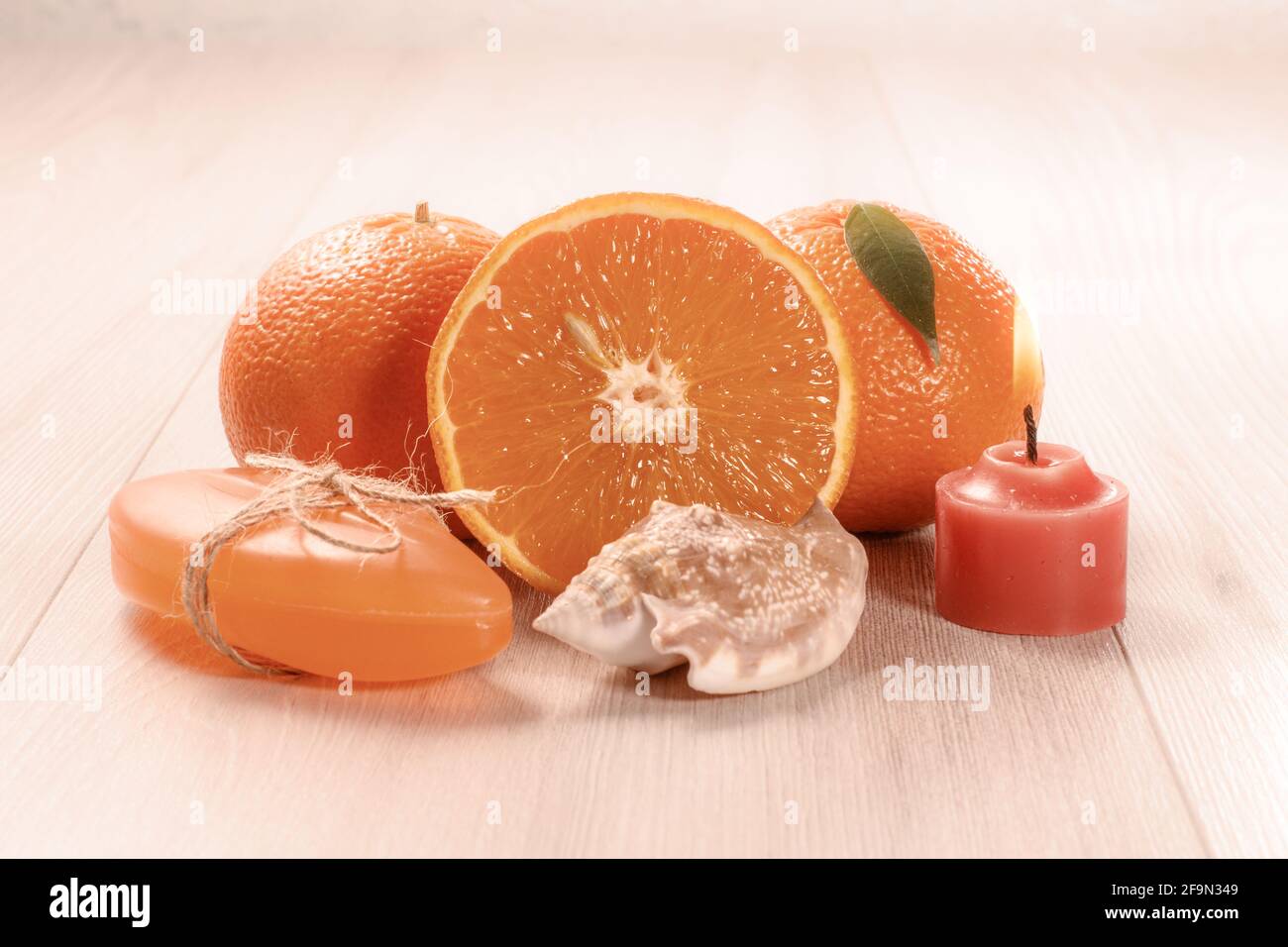 Schneiden Sie Orange mit zwei ganzen Orangen, Seife, Muscheln und brennender Kerze. Stockfoto