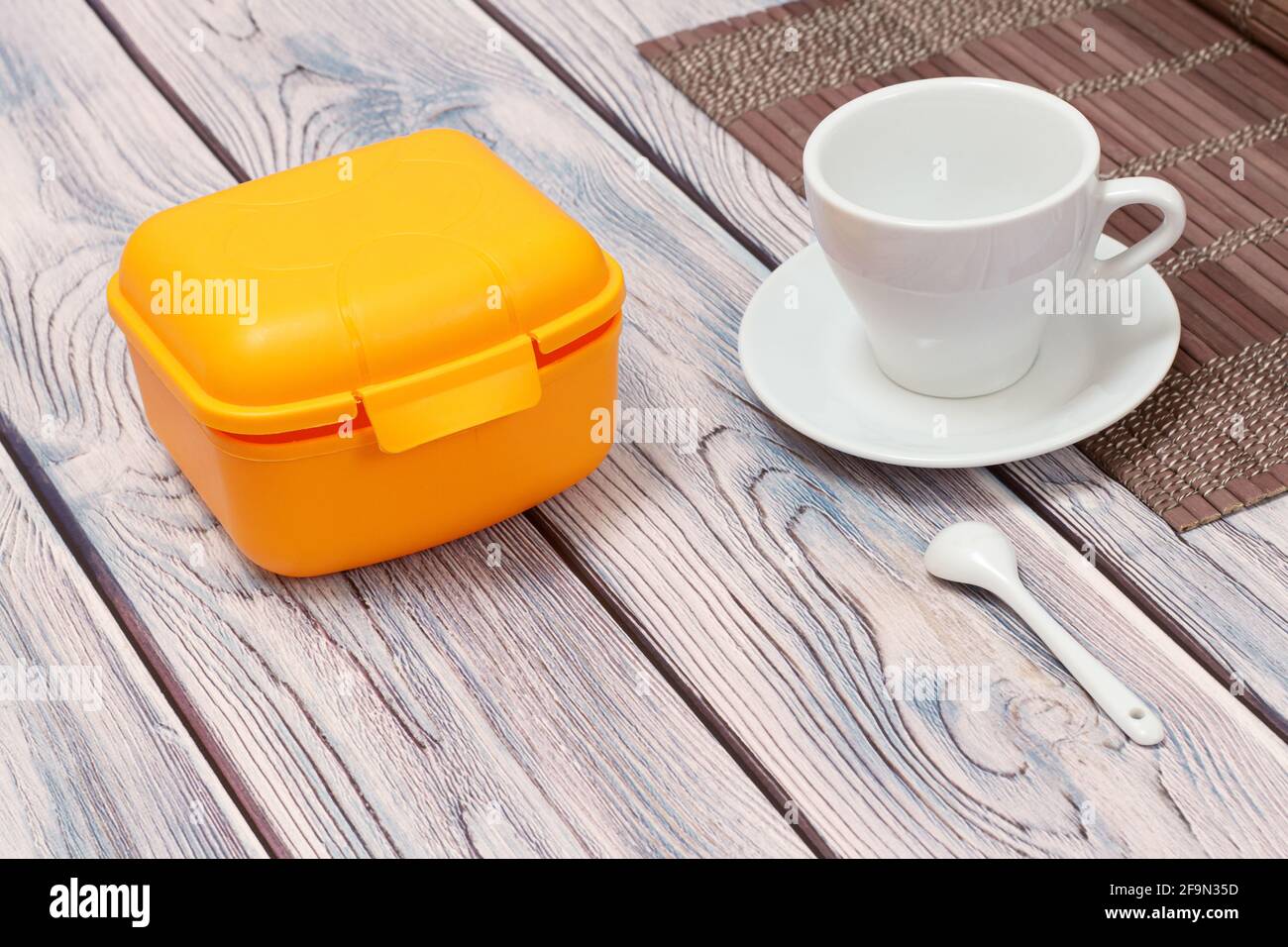 Gelbe Plastikbox und Tasse mit Untertasse auf Holzhintergrund. Stockfoto