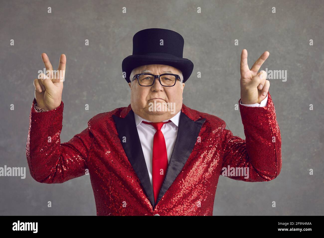 Porträt eines lustigen, seriös reichen älteren Mannes mit Zylinderhut Und Paillettenjacke mit V-Schild Stockfoto